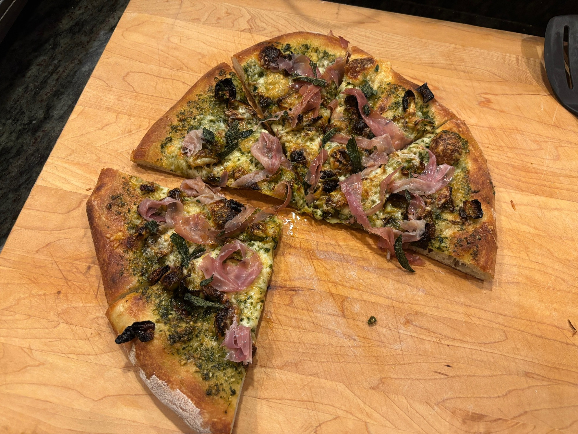 A pizza with two slices removed. It is made with Pesto, caramelized Brussels sprouts, fontina, provolone, prosciutto, crispy brown butter sage. It was yummy. 