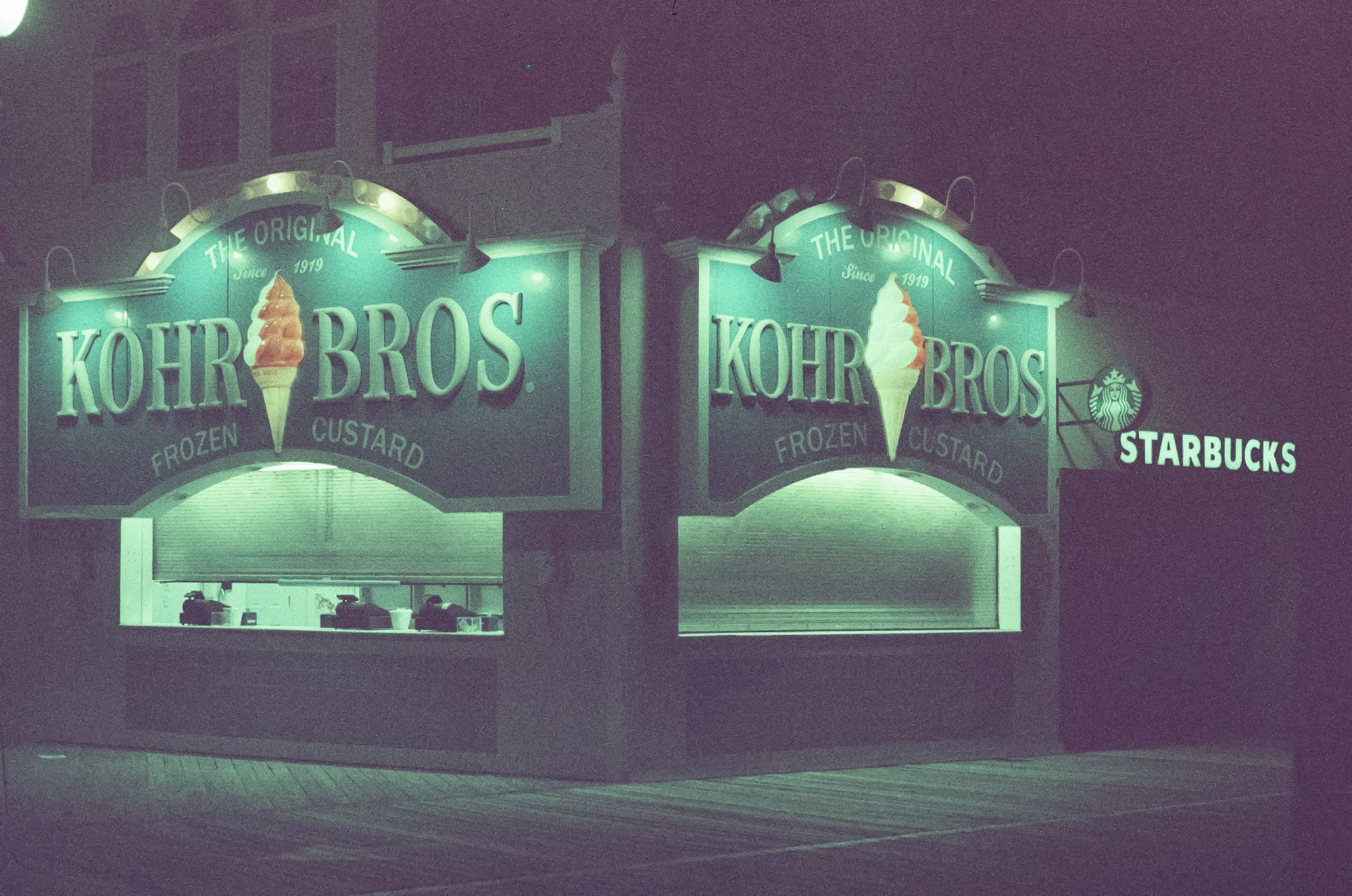 Kohr Bros. frozen custard, lit up on a dark boardwalk. To the right is a Starbucks, one of the very few national chain stores on the Ocean City boardwalk.