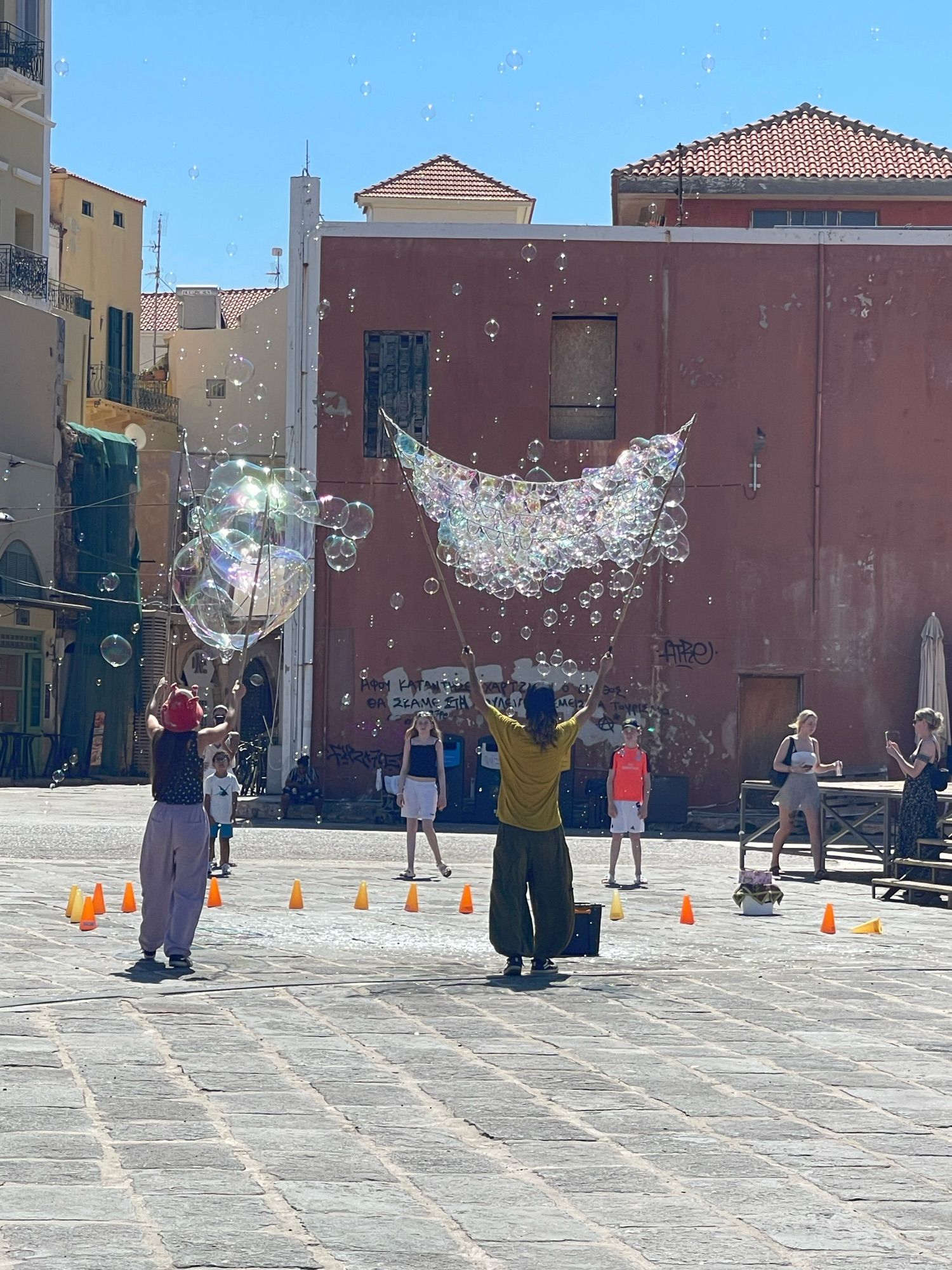 Straßenkünstler in Chania, nahe des alten Hafens, die mit langen Stöcken, Seilen und Seifenlauge riesige Seifenblasen zaubern