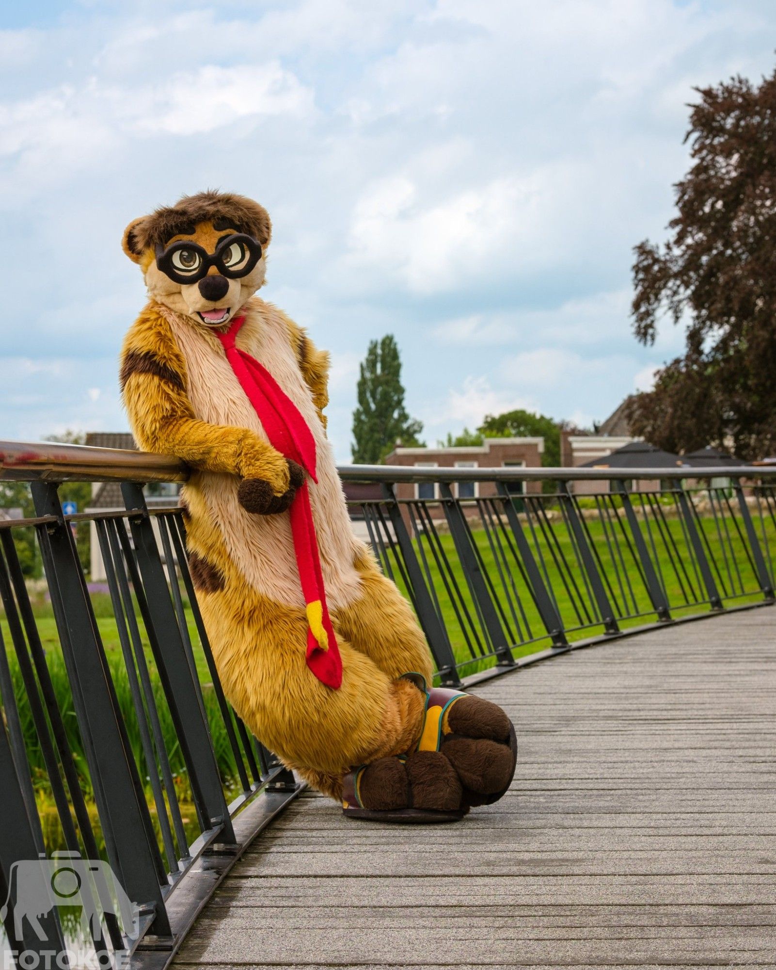 A meerkat fursuiter leaning against a railing