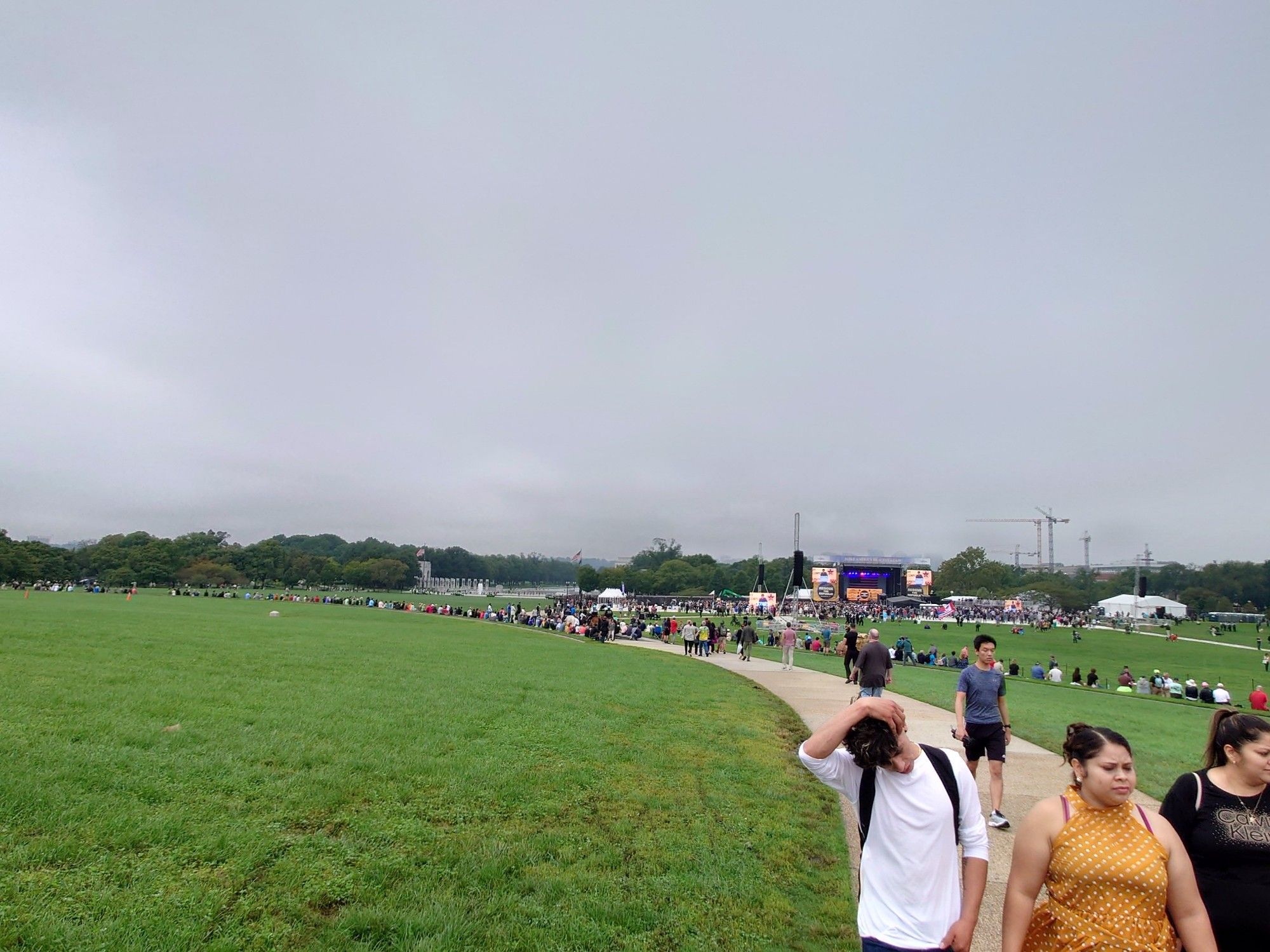 Few loose strings of people behind a larger but still modest crowd in front of a stage