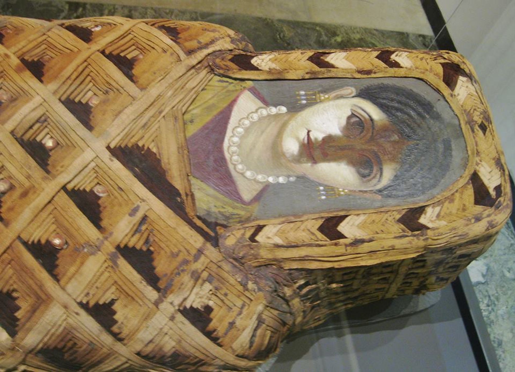 Portrait d'une jeune femme coiffée et parée de bijoux de perle, à la mode romaine.
Le portrait a été peint sur une planche en bois pour être placé au niveau de la tête du défunt, sur son sarcophage.