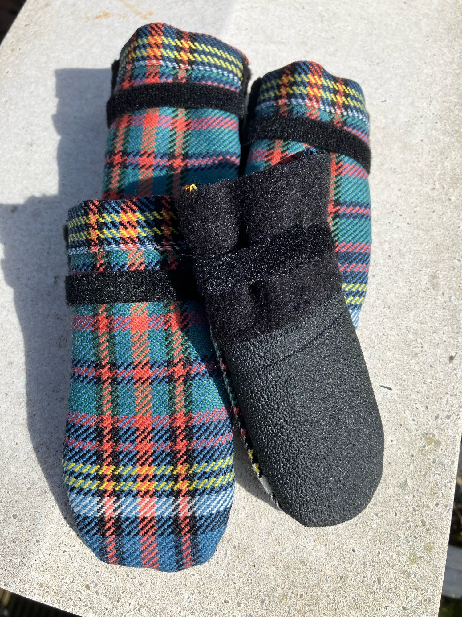 Four dog booties, one showing the underside, in Anderson tartan (ancient) green, blue, black, yellow,white and and odd shade of red/orange.