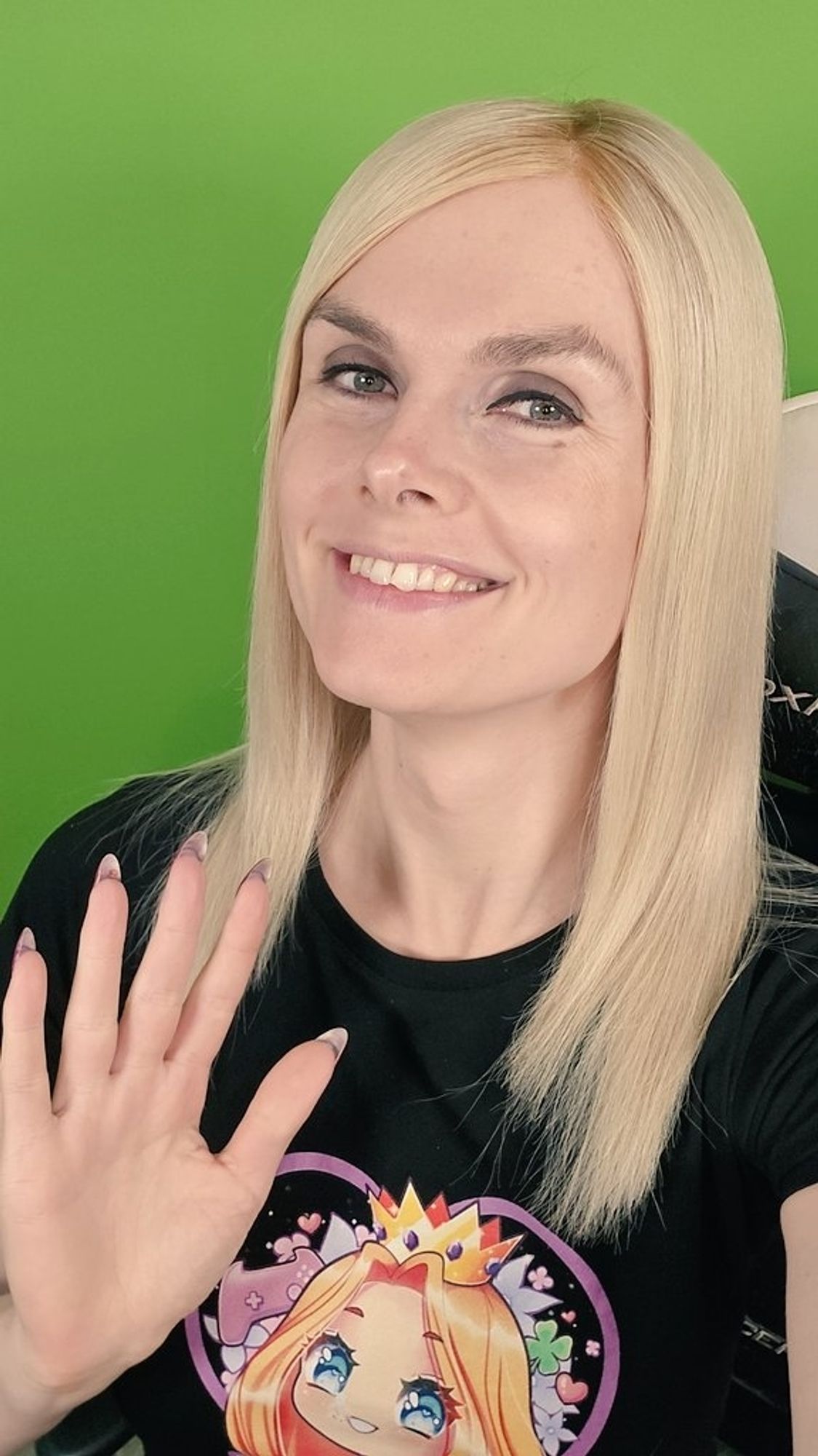 Lena lächelnd vor ihrem Greenscreen. Sie hebt die rechte Hand und trägt ein schwarzes Shirt mit Lalena Logo darauf