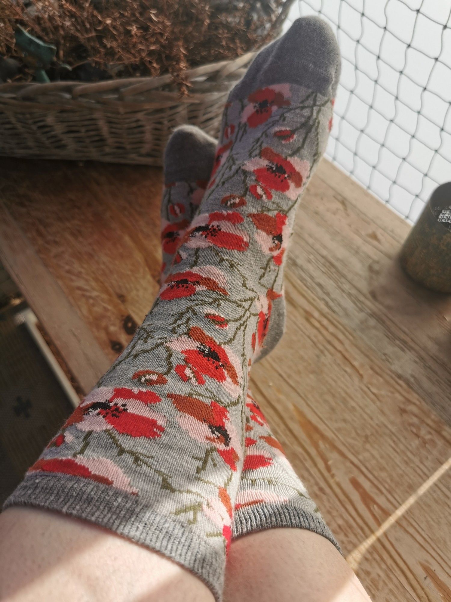 Zu sehen sind meine Füße, abgelegt auf einer Holzbank. Ich trage Socken mit Mohnblumen darauf!