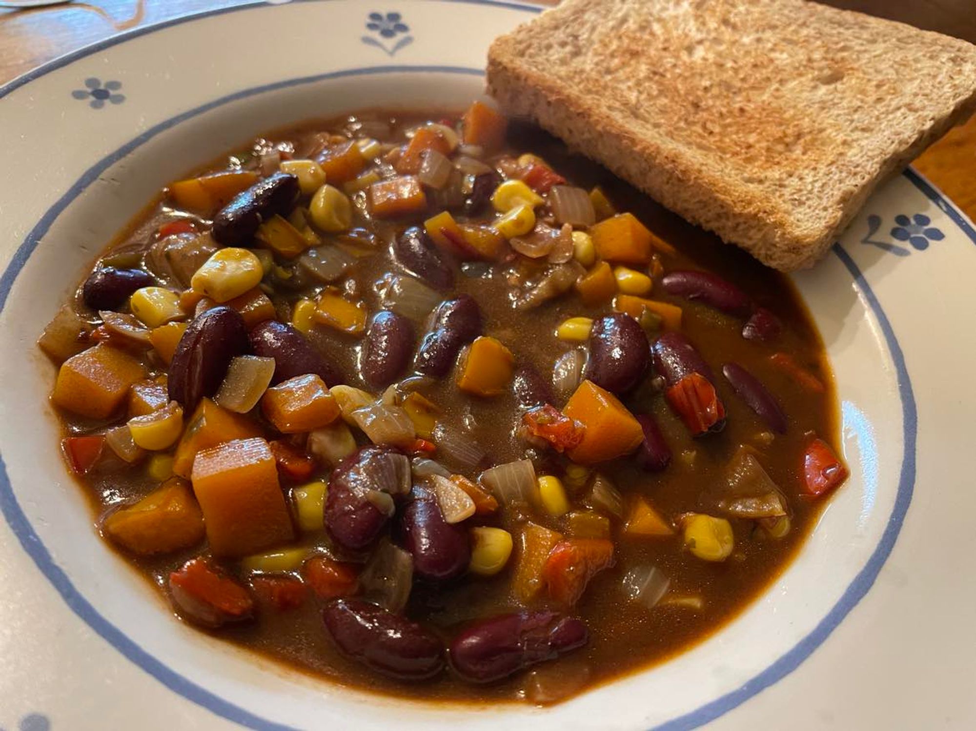 Chilli in tiefem weißen Teller mit blauen Blümchen, an der Seite eine Scheibe Toast, getoastet