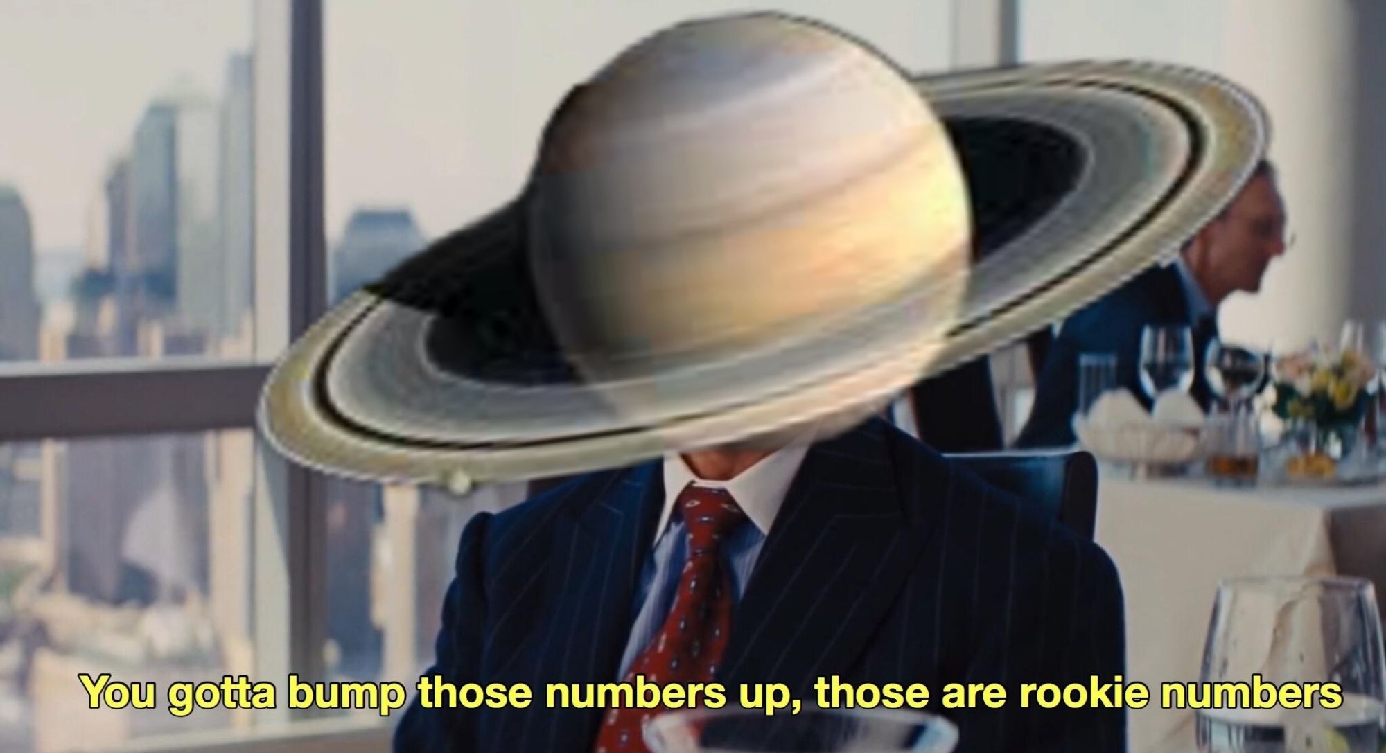 matthew mcconaughey from "the wolf of wall street" (2013) sitting down wearing a suit and tie, his head has been replaced by the planet Saturn. 
Caption at bottom: "You gotta bump those numbers up, those are rookie numbers"