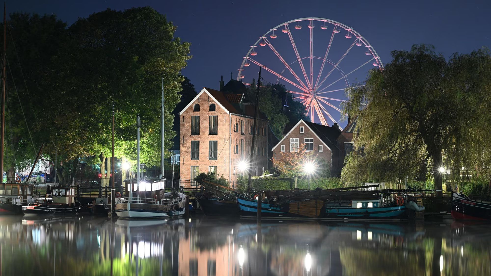 Kurz vor dem Sonnenaufgang: Museumshafen in Leer, im Vordergrund alte Schiffe, dahinter Häuser und hinter diesen sieht man das Riesenrad. Es gehört zum Gallimarkt, der am Mittwoch startet.