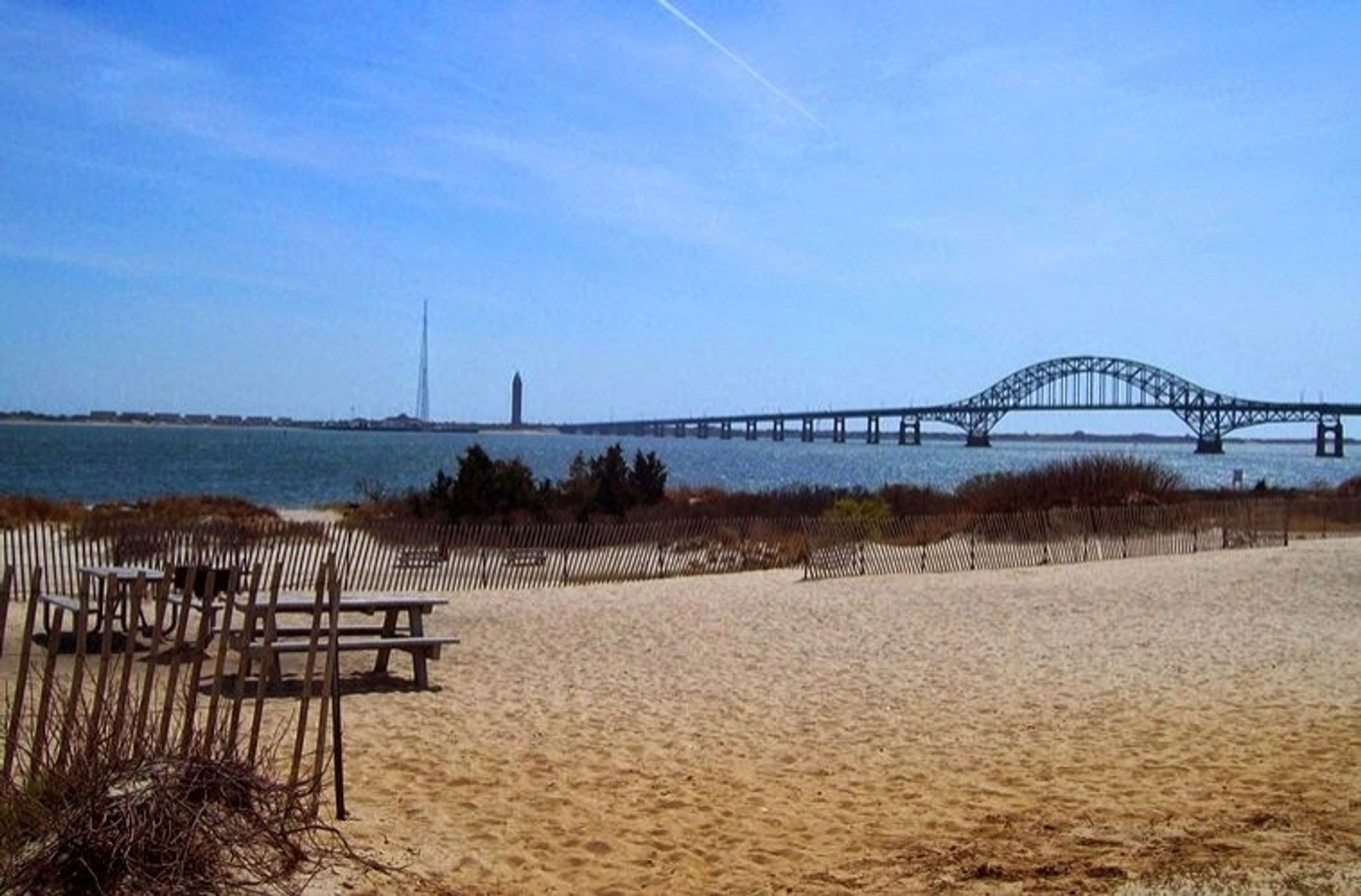 A bridge on the right side over the water. Picnic tables on the left side.