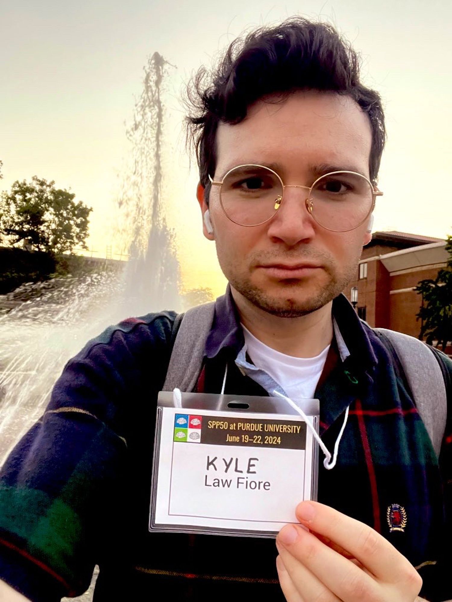 Me, Kyle, with my name tag prominently displayed while standing in front of a fountain wearing a vintage, plaid Tommy Hilfiger polo on a hot June afternoon at Perdue University.