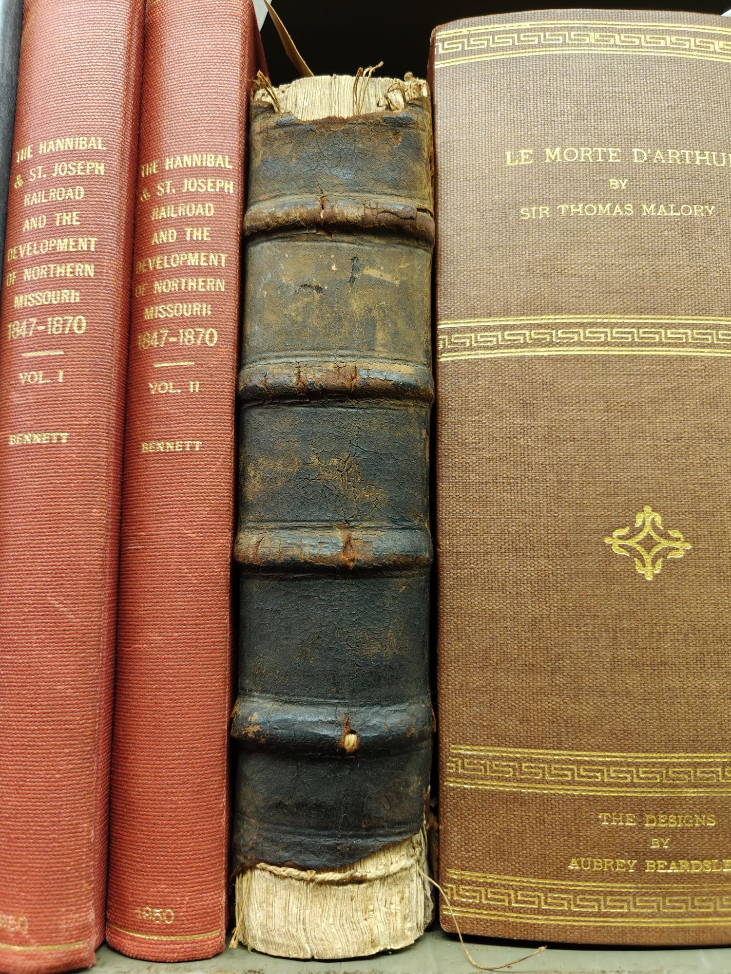 Leatherbound book with spine compartments and headbands missing, peeking out from between two others on the shelf