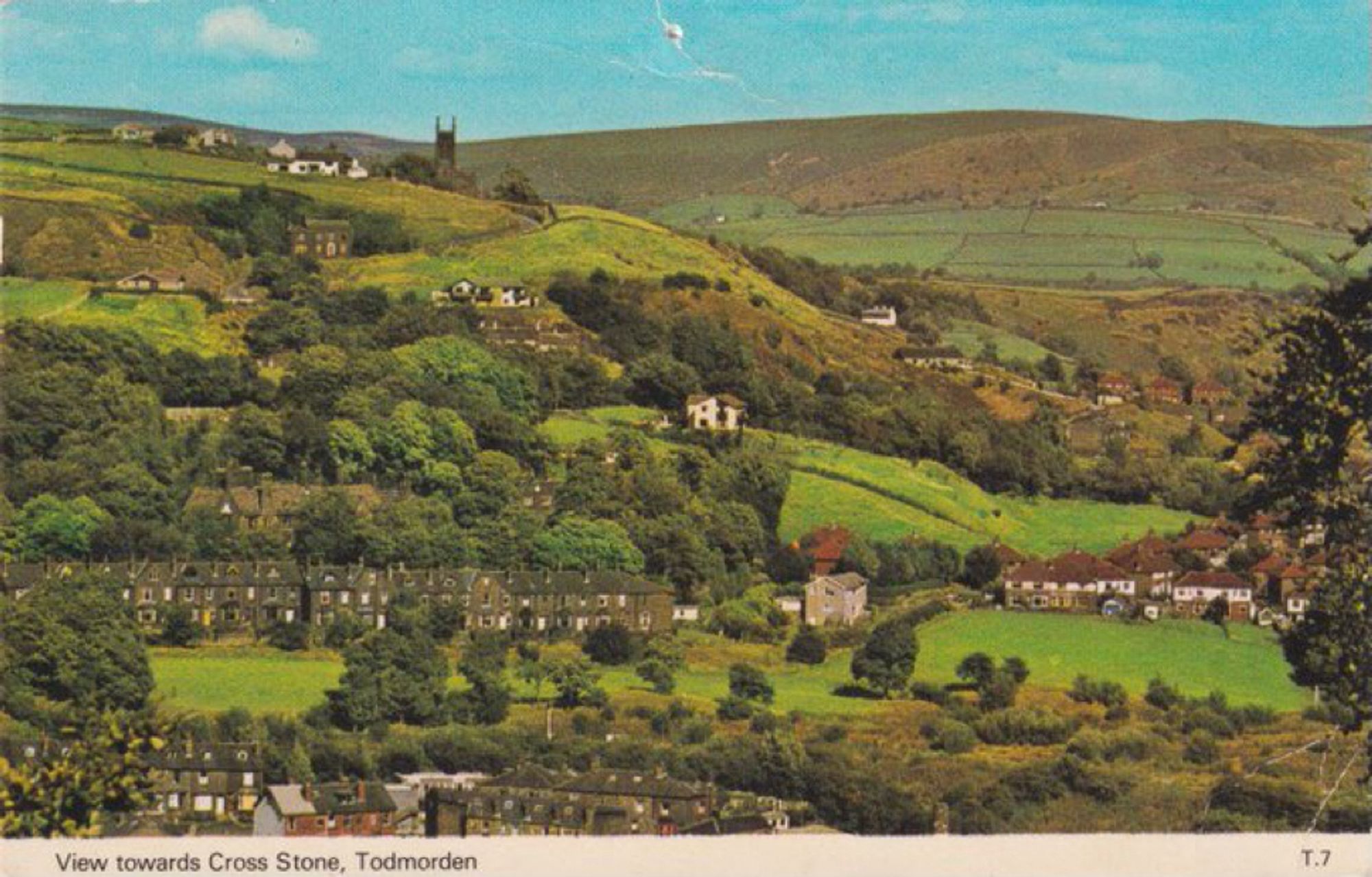 A postcard style photograph taken on a sunny day looking back at the town of Todmorden in West Yorkshire, England