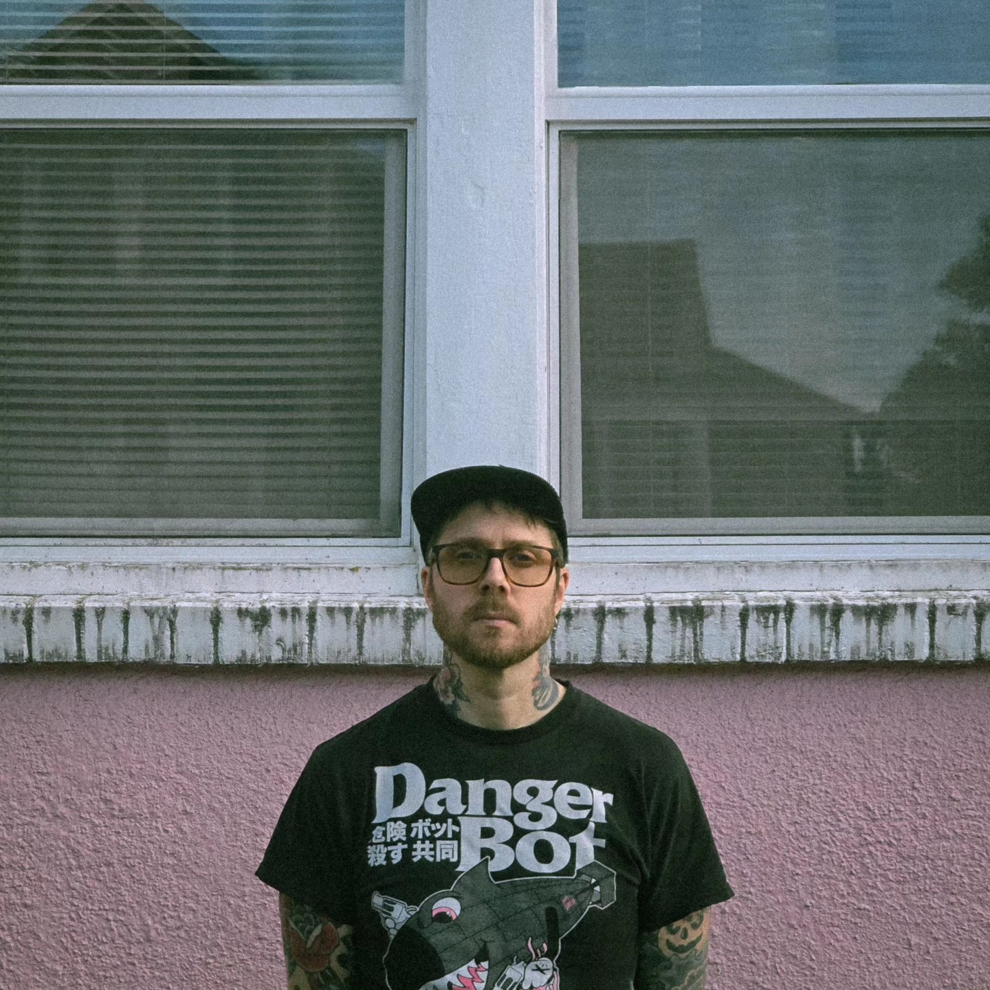 white dude standing in front of a pink house with dingy windows