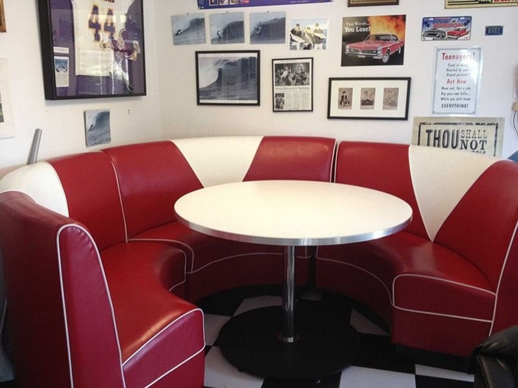 A 60's American Diner (My refrence image/original version)

3 red curved booth chairs with white triangles in the middle. Small white table in the middle of the chairs. Checkered floor. Photos and frames hung on the pale white wall few being photos of someone surfing, a 60's red car, newspaper, sports team shirt with the rewards in a frame, and small photos of 3 people.