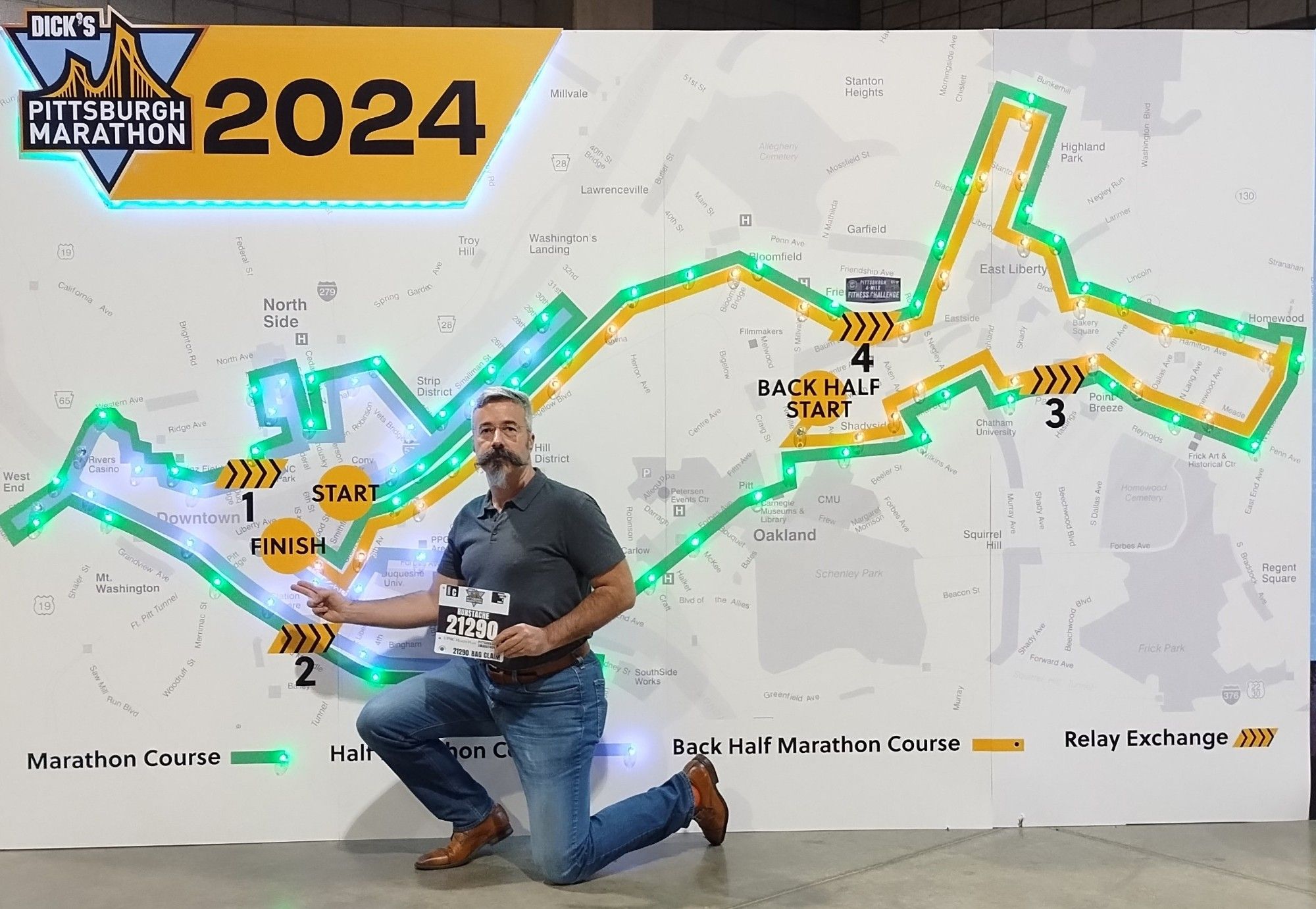 Tom kneels in front of the map of the Pittsburgh Marathon.