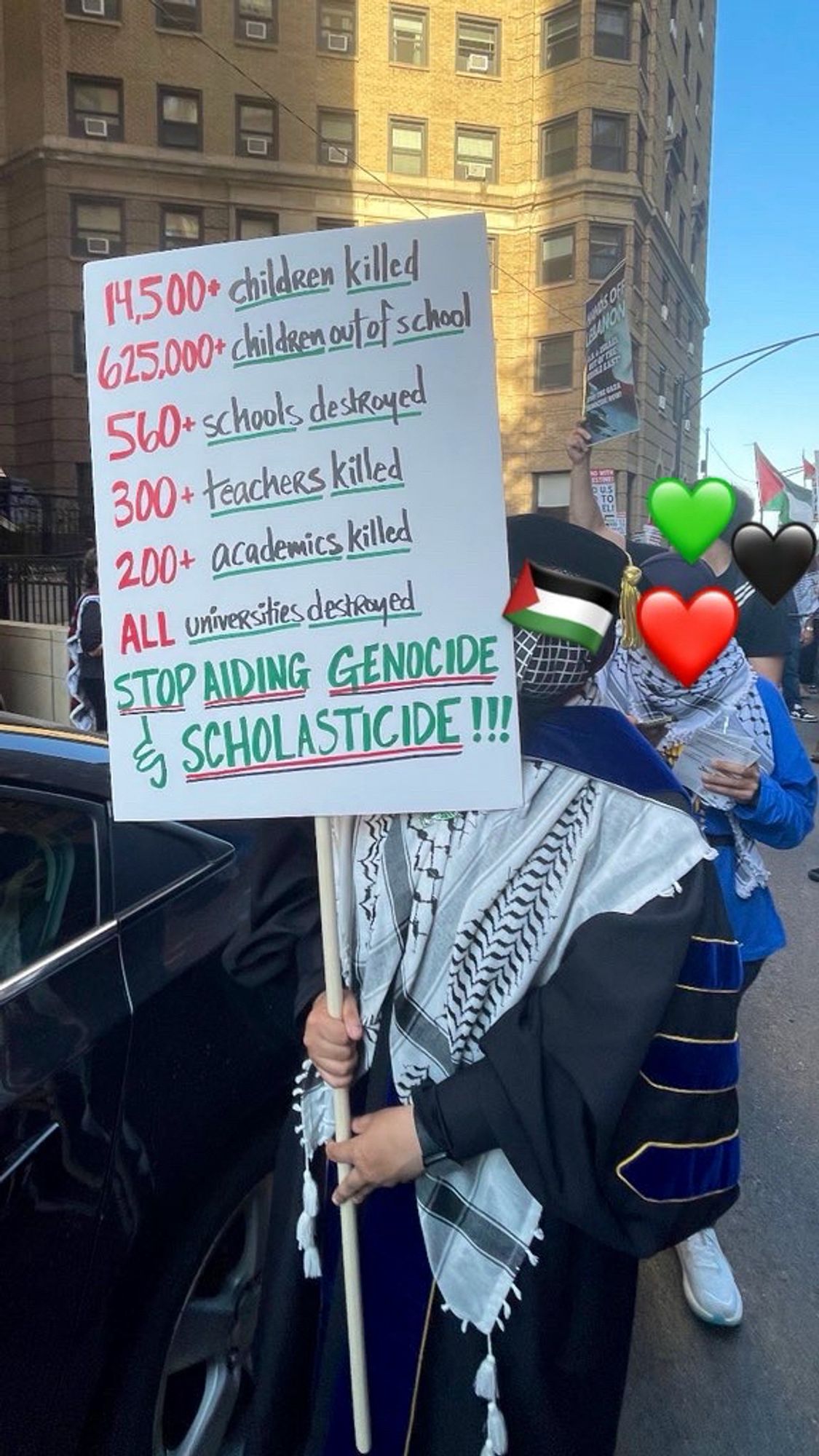 A person in academic regalia and N95 mask carrying a poster at a Palestinian liberation & anti genocide protest. The poster reads:

14,500+ children killed
625,000+ children out of school
560+ schools destroyed
300+ teachers killed
200+ academics killed
ALL universities destroyed
STOP AIDING GENOCIDE & SCHOLASTICIDE!!!