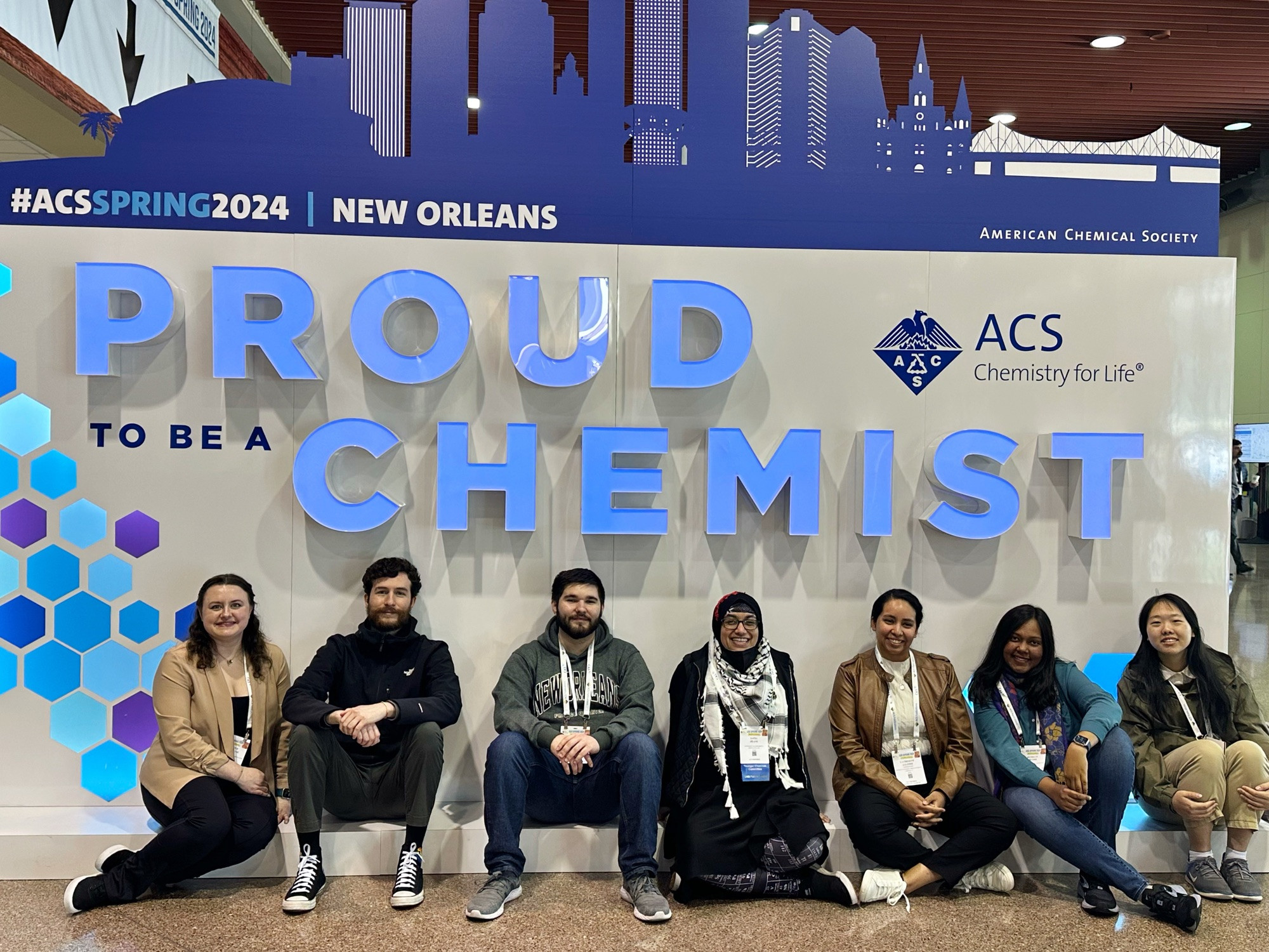 7 early career scientists from the NSF Center for Sustainable Nanotechnology sitting in front of the “Proud to be a Chemist” sign at ACS Spring 2024