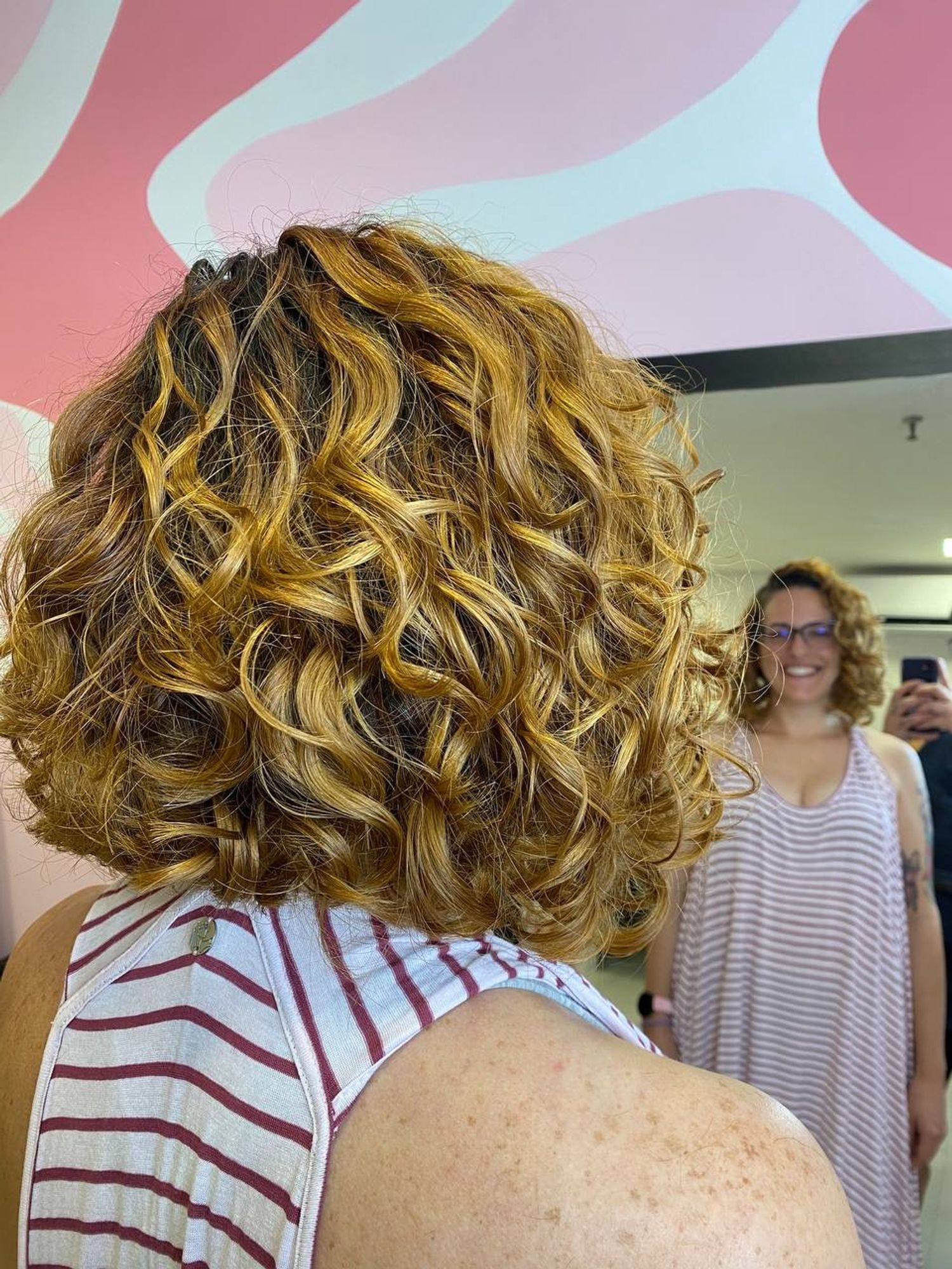 Mulher ruiva, de cabelo ondulado na altura da nuca, de frente para o espelho e sorrindo.