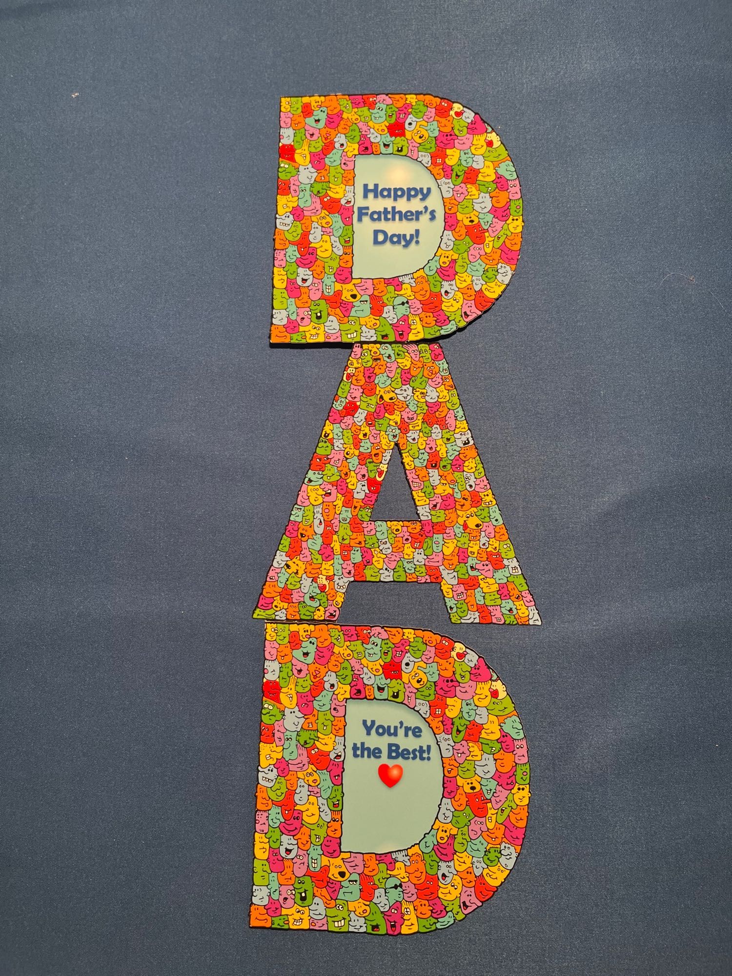 A colorful greeting card of die-cut letters that spell DAD made up of hundreds of colorful cartoon faces. 