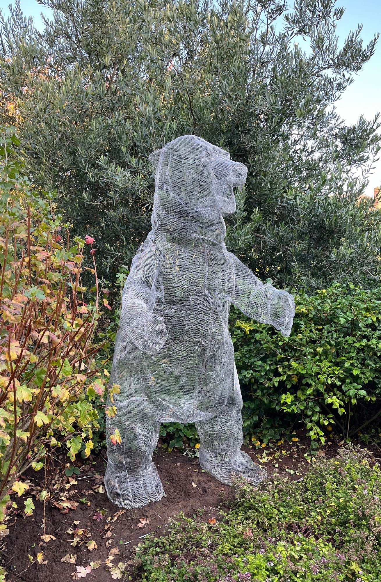 Life size wire work brown bear standing on hind legs with mouth open and looking angry, he’s standing amongst shrubs and planting in a park