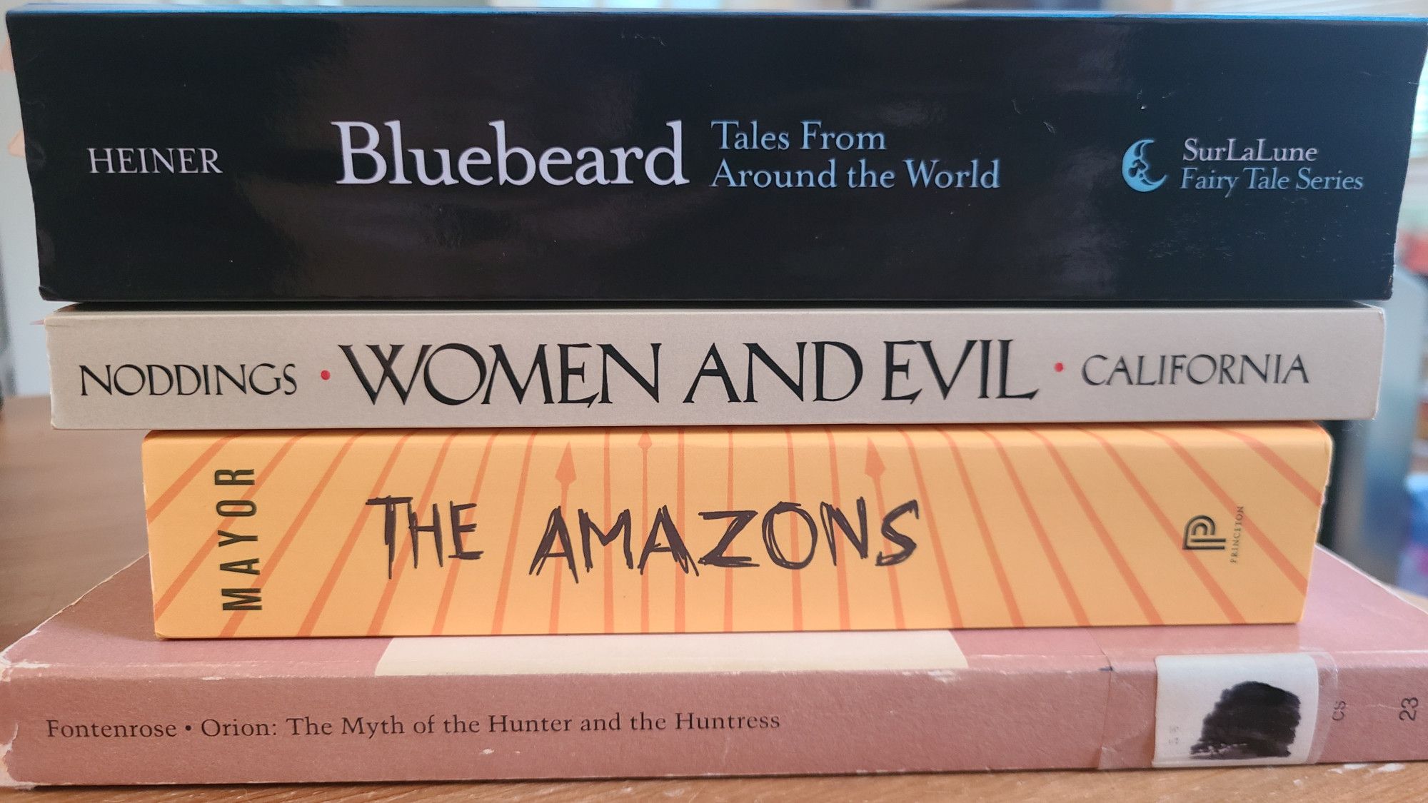 Pile of 4 books: Bluebeard Tales From Around the World, Women & Evil by Nel Noddings, The Amazons by Adrienne Mayor, and Orion: The Myth of the Hunter and the Huntress by Joseph Fontenrose