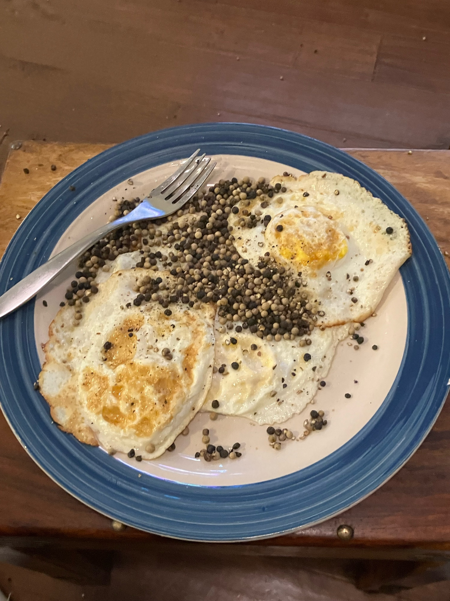 A plate featuring three fries eggs an entire grinder’s worth of peppercorns 