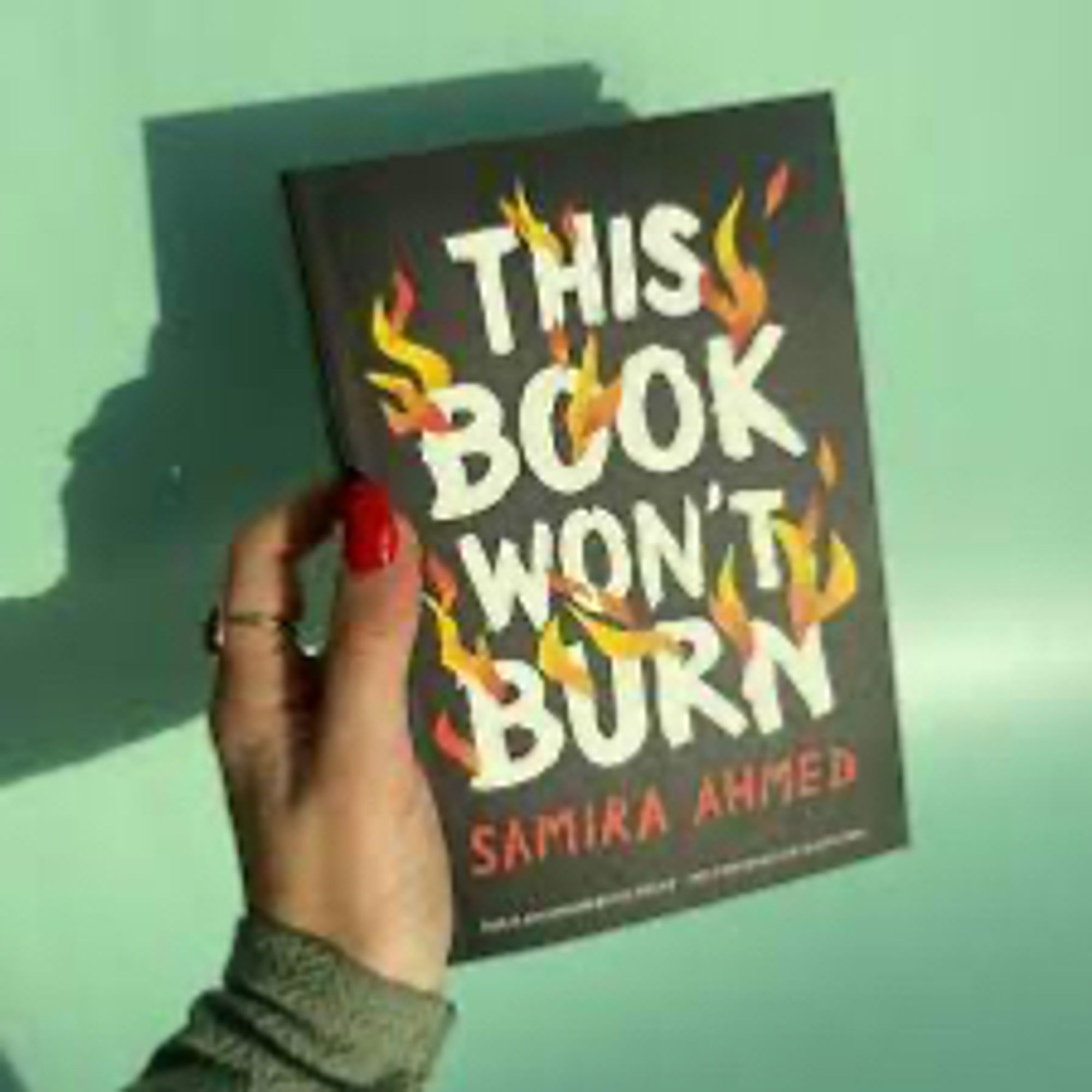 Samira Ahmed holding her new book, which has a black cover, and the words This Book Won’t Burn in white letters, with flames layered on top and through the lettering.