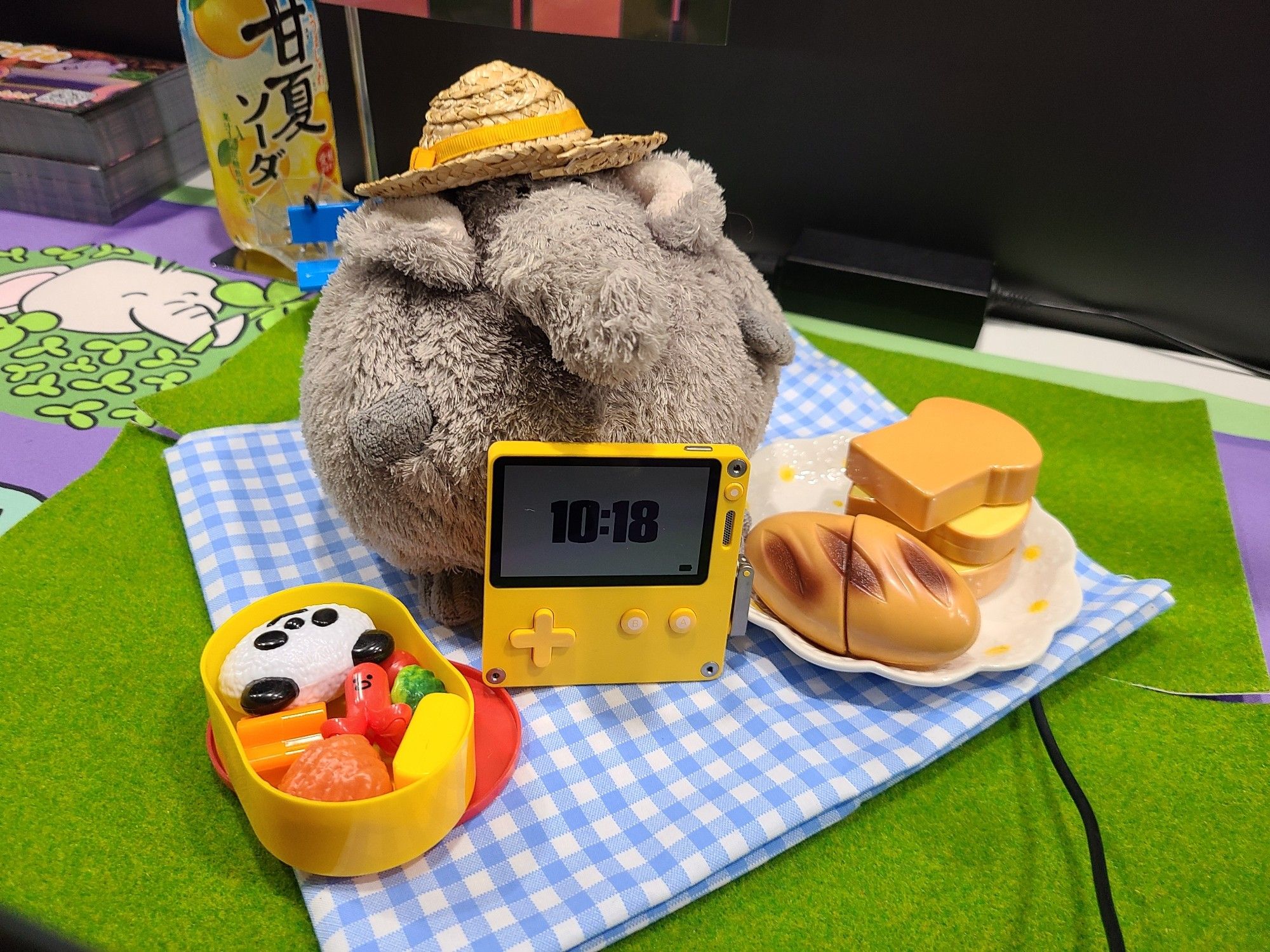 Elfie a stuffed elephant sitting on a gingham check blanket and having a little picnic with a Playdate console