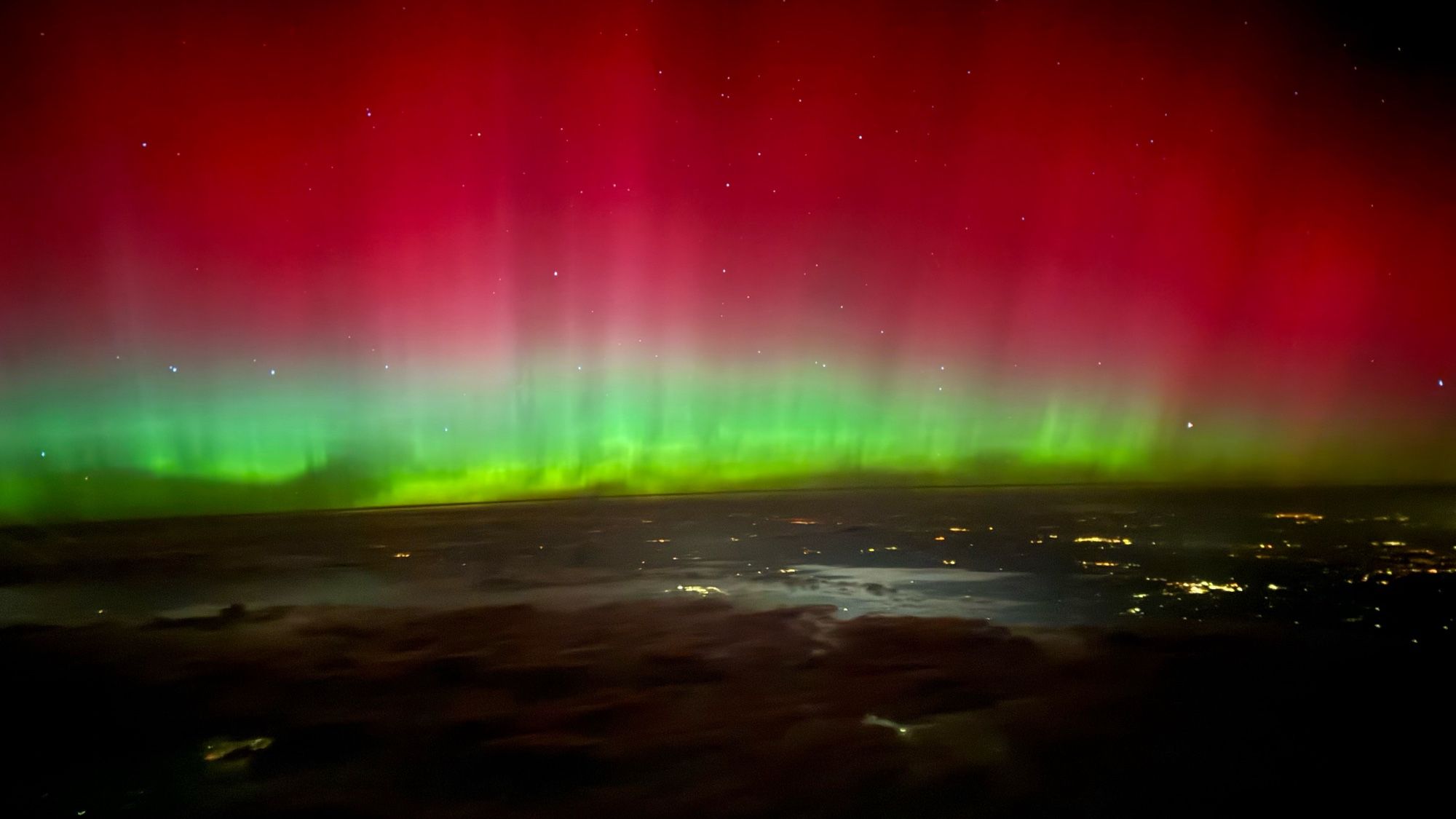 Swirling green and red aurora above city lights with stars shining through