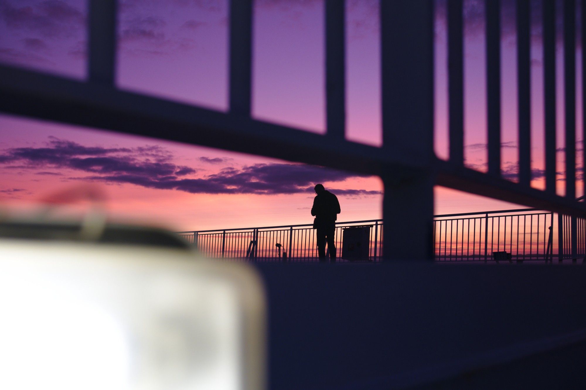 Silhouette of a man against a colourful sunset, the frame is structured by railings and a brightly lit light.