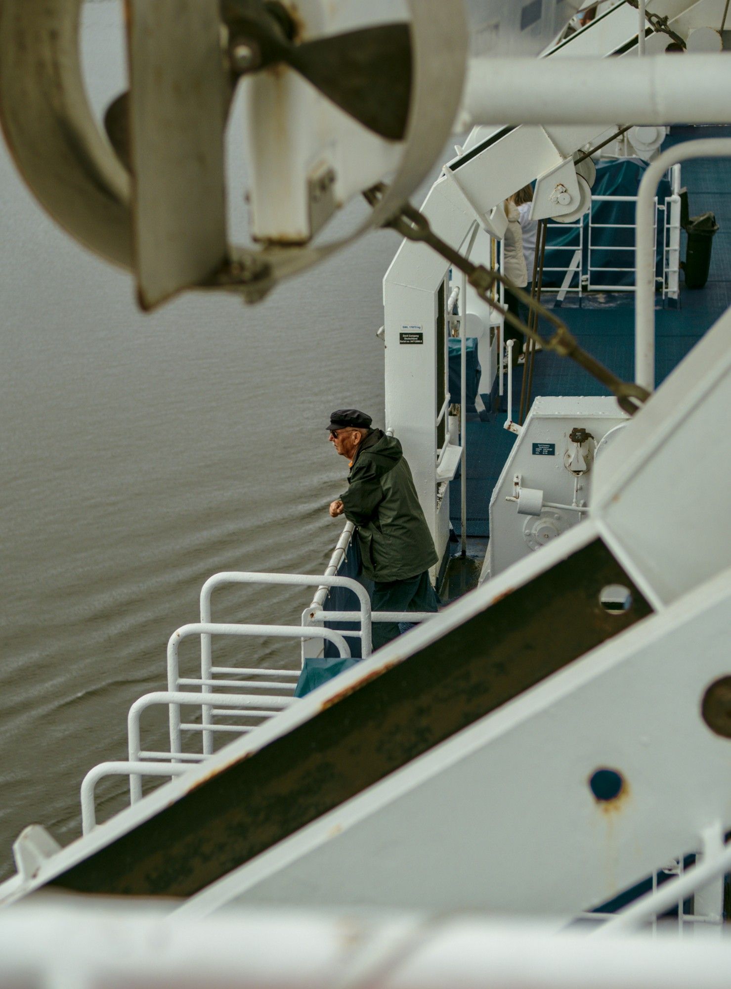 A man onboard a North Sea ferry, looking over the grey water into the distance. He is framed by a lifeboat at the top and steel beams at the bottom.