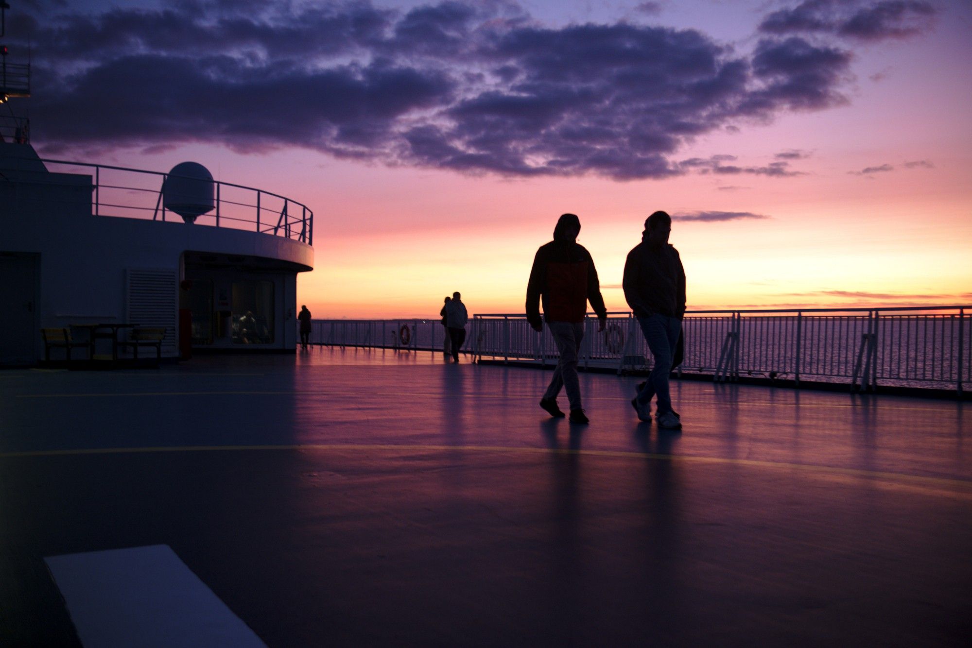 Silhouette of several persons against a colourful sunset, behind them the sea and the horizon.