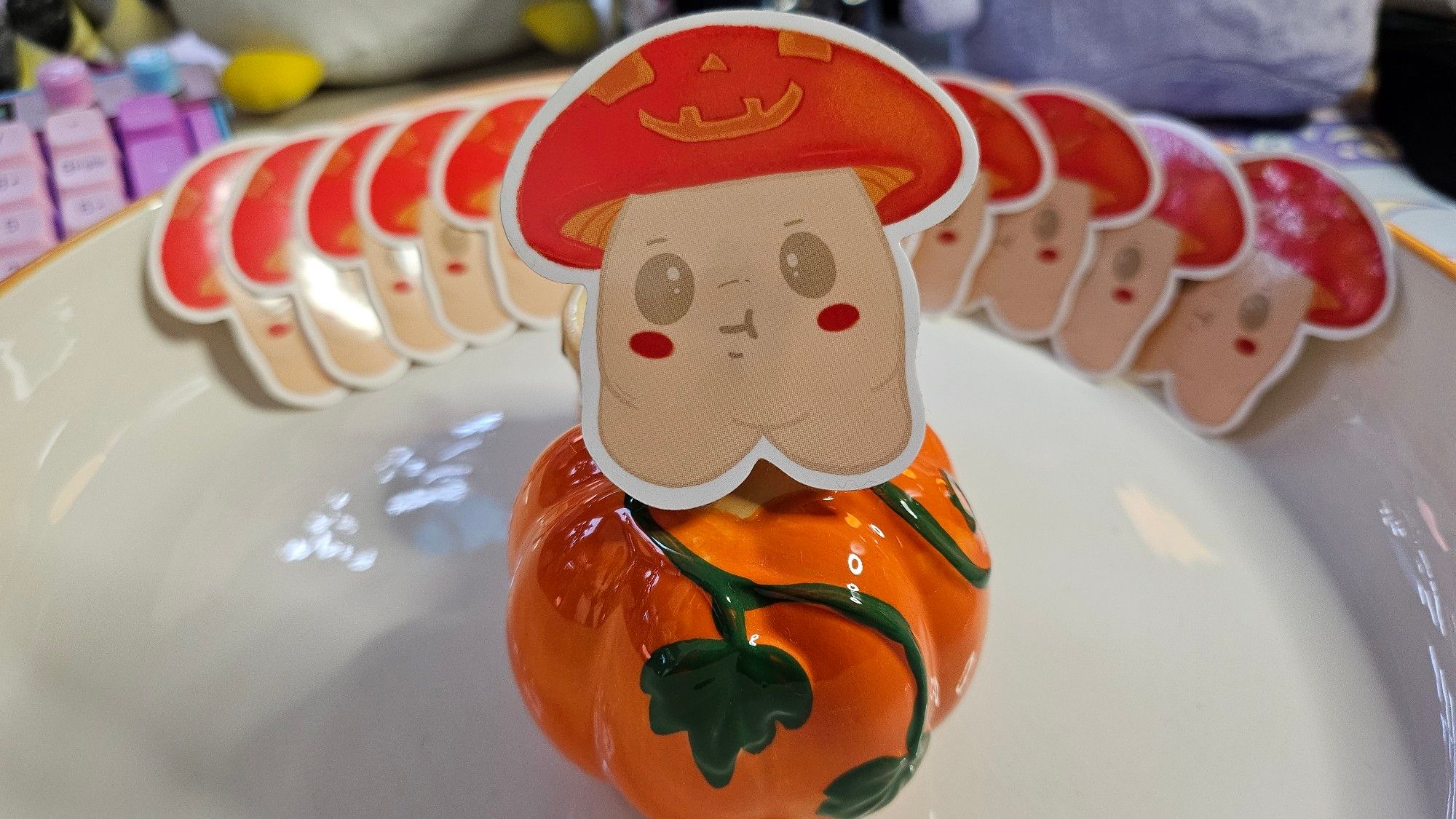 A die-cut sticker of a cute little mushroom person. Their colours are like a red cap mushroom, but the top has a pattern on it like a Halloween pumpkin lantern