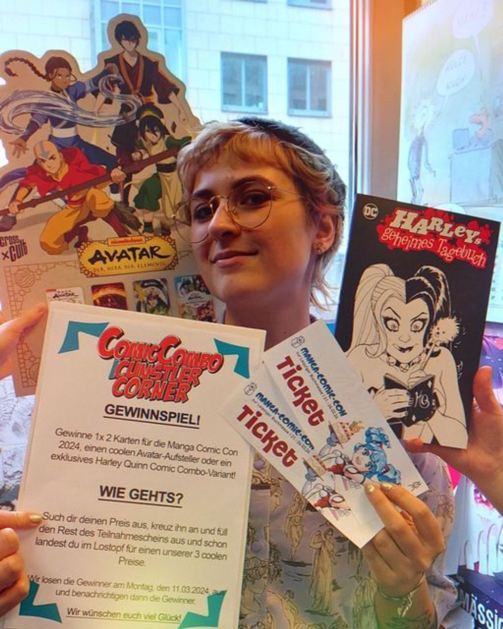 Eine Erklärung für ein Gewinnspiel wird in die Kamera gehalten, zusammen mit den Preisen, wie Tickets für die Manga Comic Combo, ein Variant und ein avatar-Aufsteller