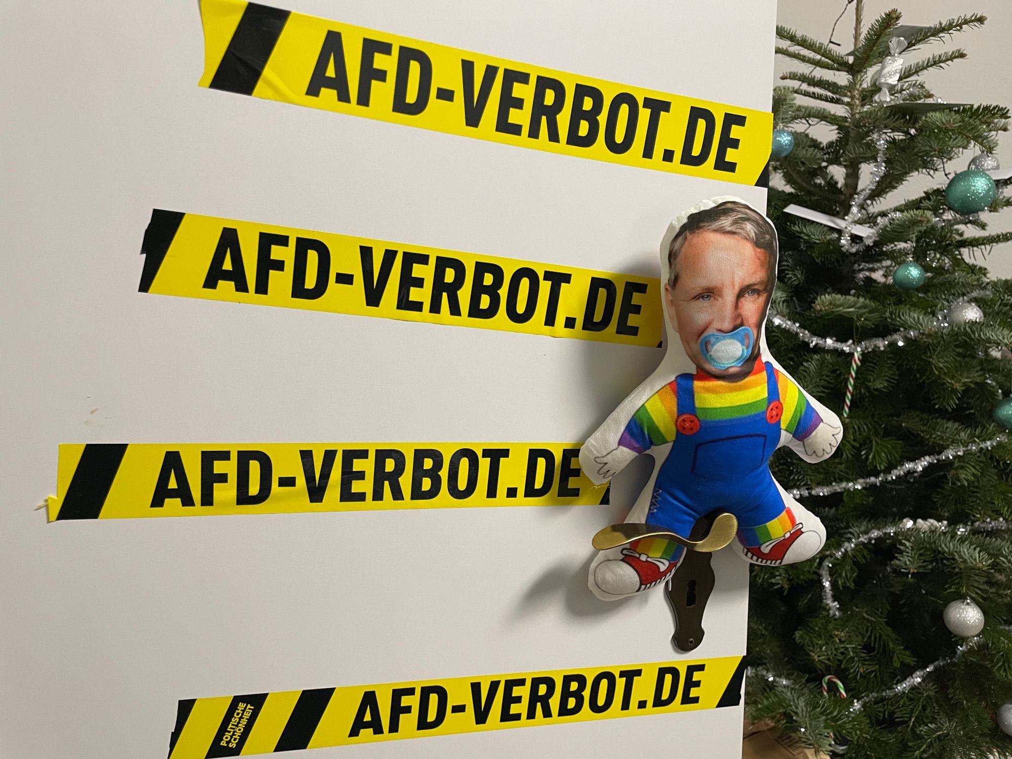 Eine Puppe mit Schnuller im Mund und Band, auf dem AfD-Verbot.de steht.