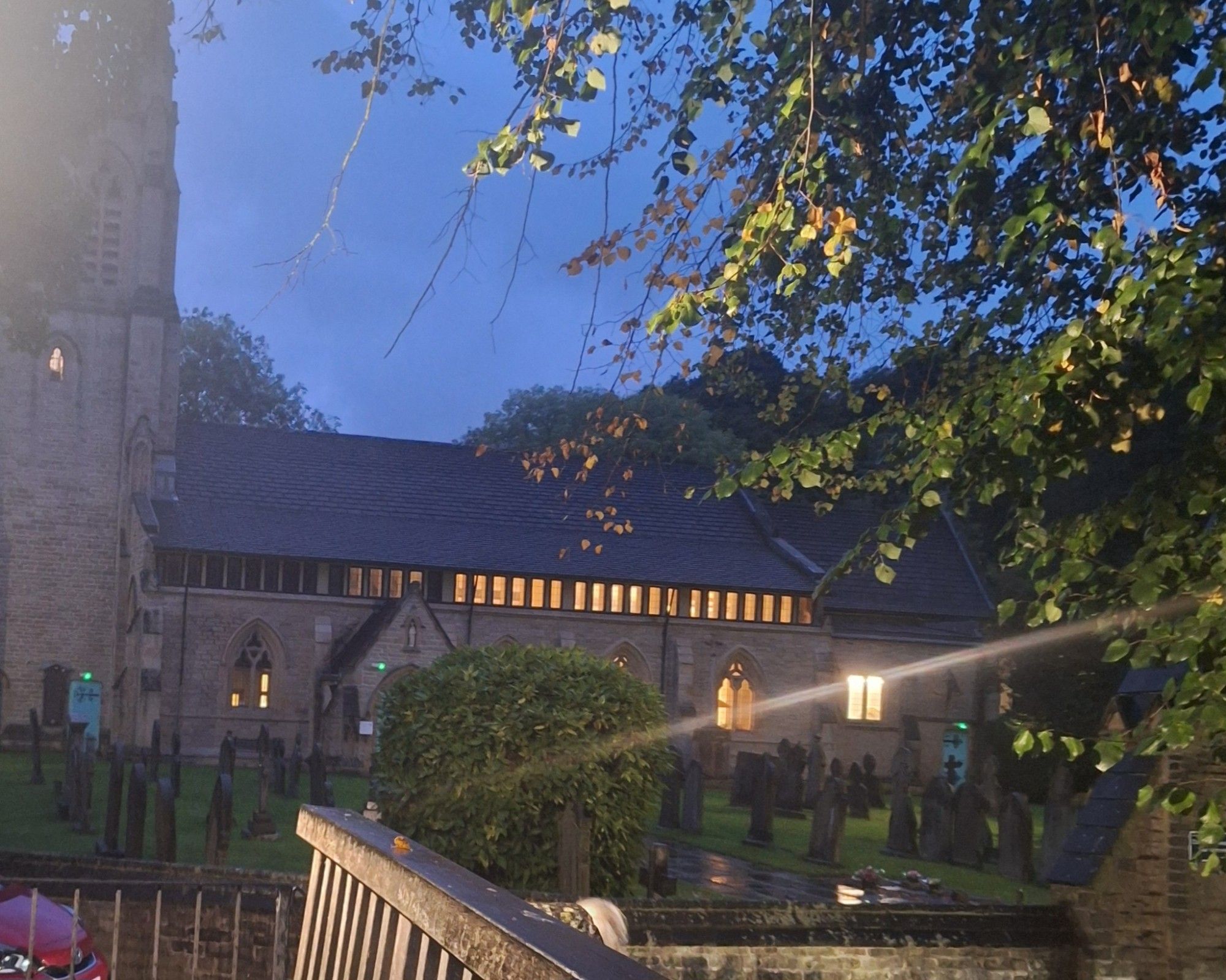 The church of St Paul's Armitage Bridge taken from the footbridge over the River Holme. The church has its lights on, which glow in the semi-darkness