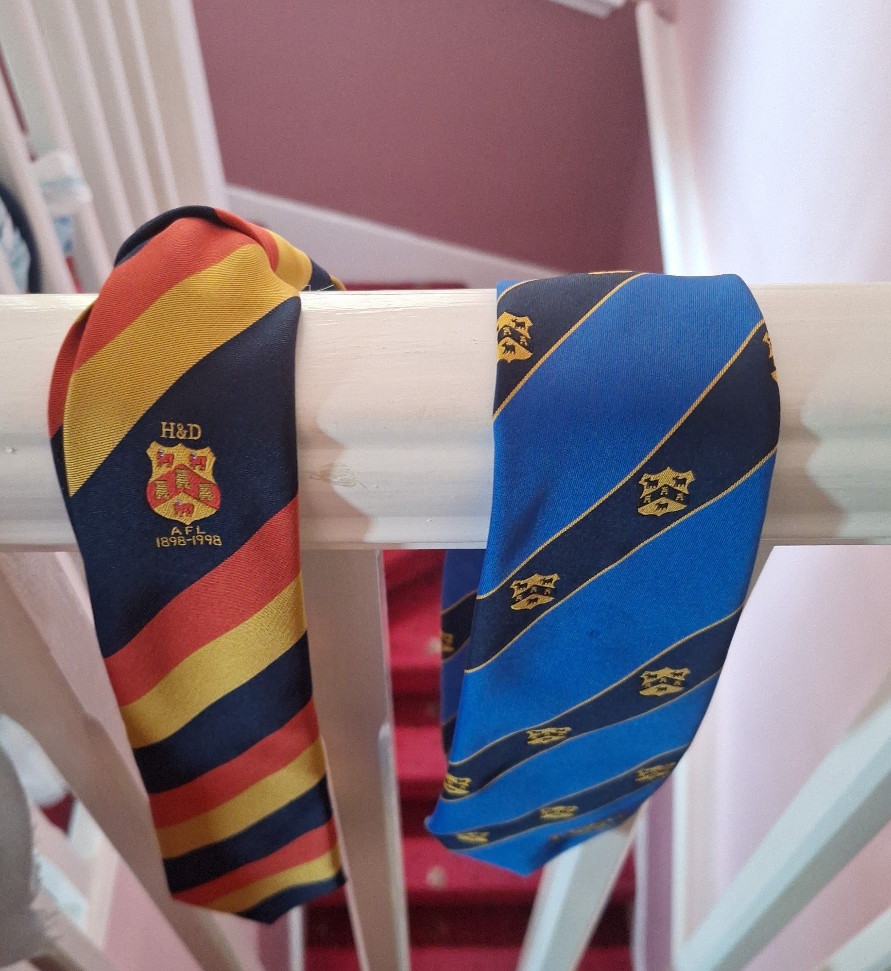 Two ties, one striped red, yellow, and black, and one striped light blue and navy with yellow crests of the Hudderfield and District Football Association