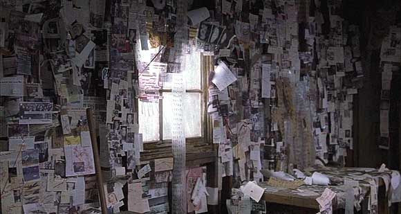 A entire wall covered with all different kinds of papers taped up, and a long paper tape covered with numbers hanging across a window.