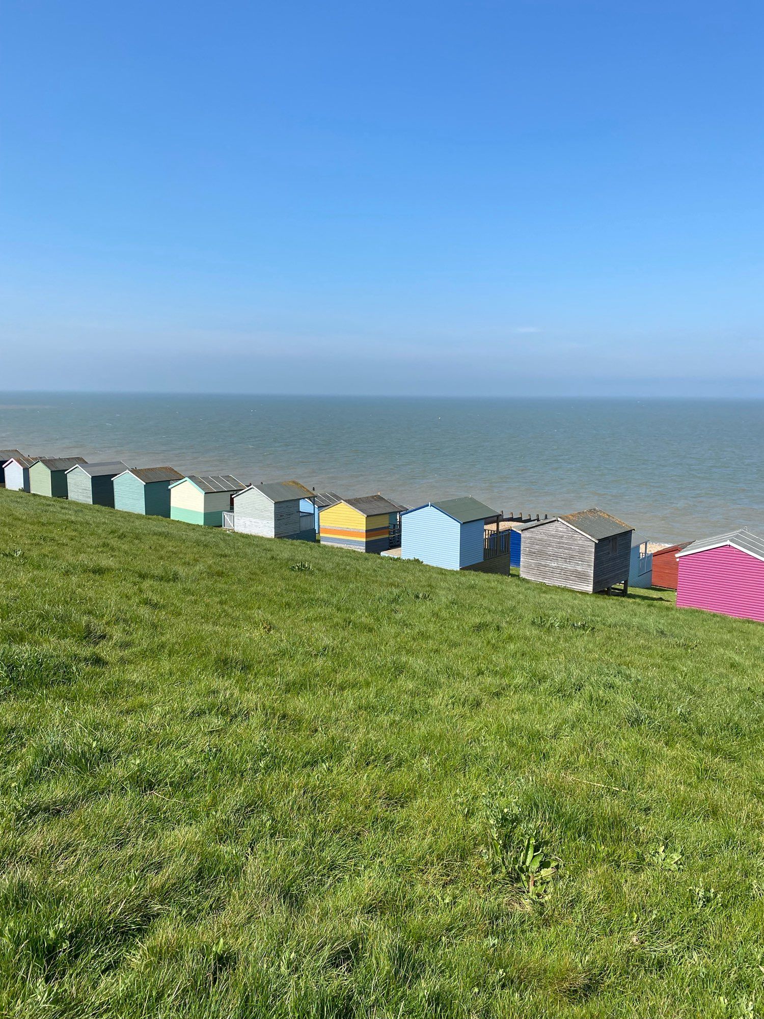 Von einer Wiese Blick aufs Meer. Farbige strandhäuser stehen in einer Reihe