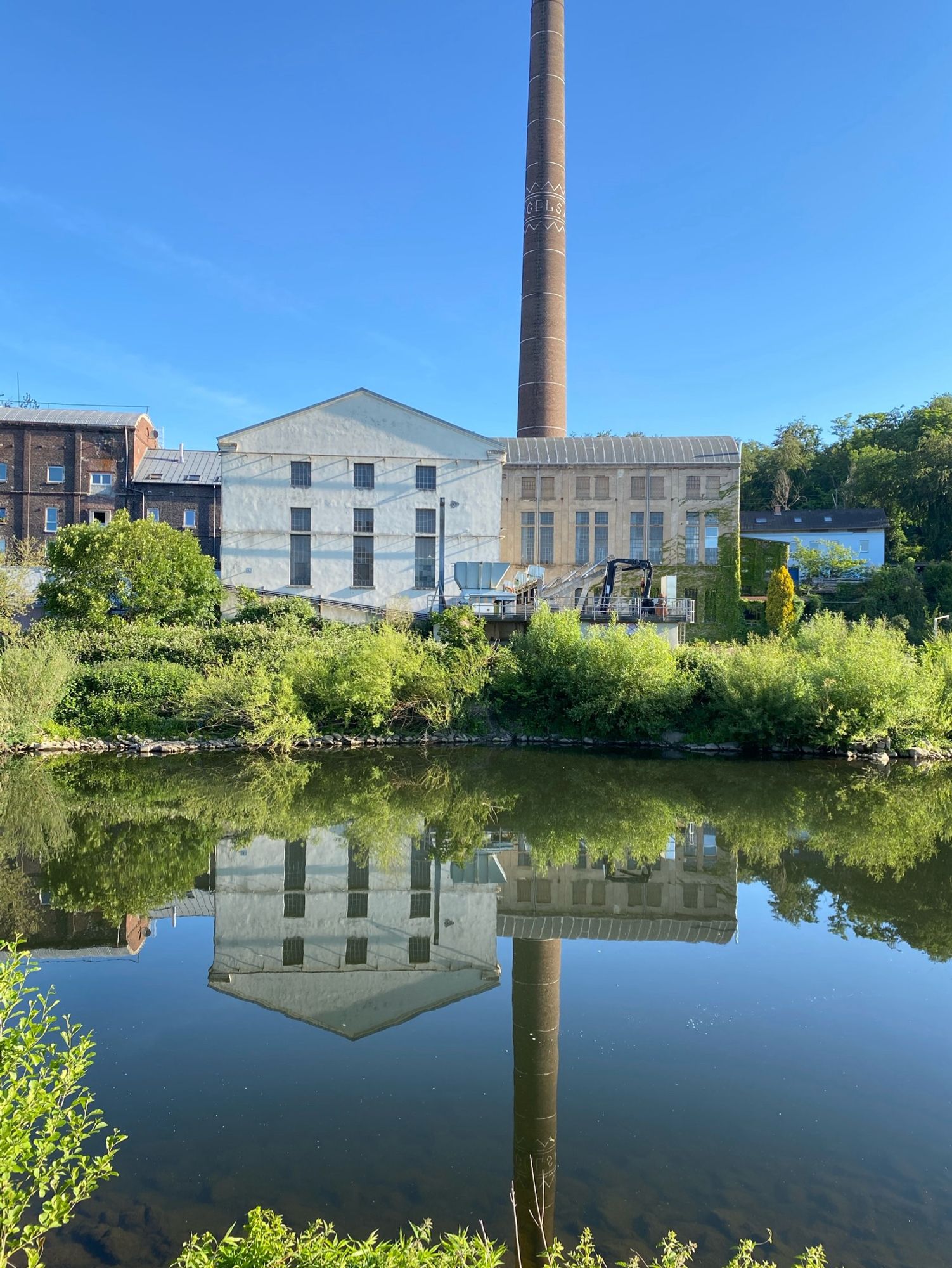 Ein altes Fabrikgebäude mit Industrieschornstein dahinter spiegelt sich in der Ruhr