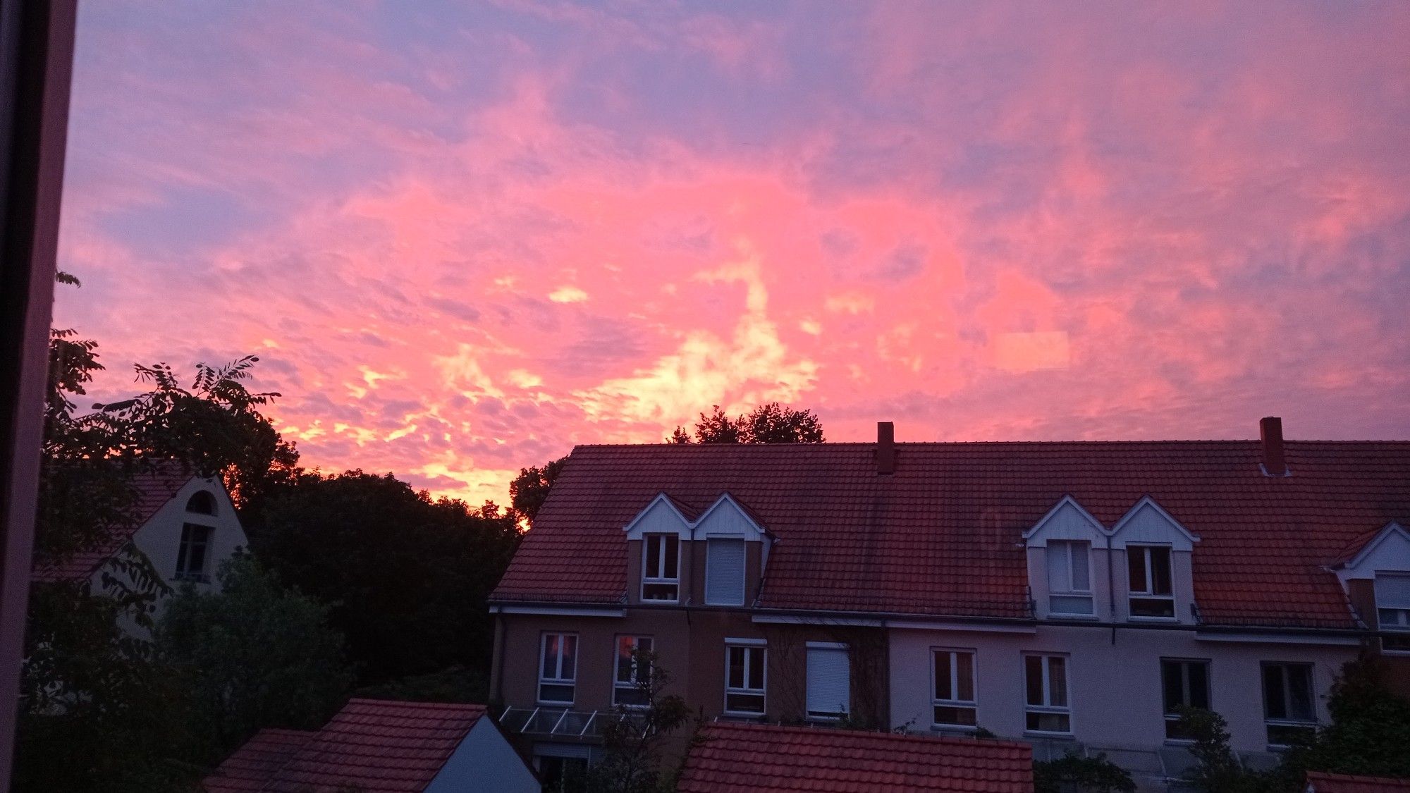 In der unteren Hälfte ist eine Häuserfront mit roten Ziegeln zu sehen. Darüber ein scheinbar brennender Himmel in verschiedensten Töten von rot, lila, und gelb.