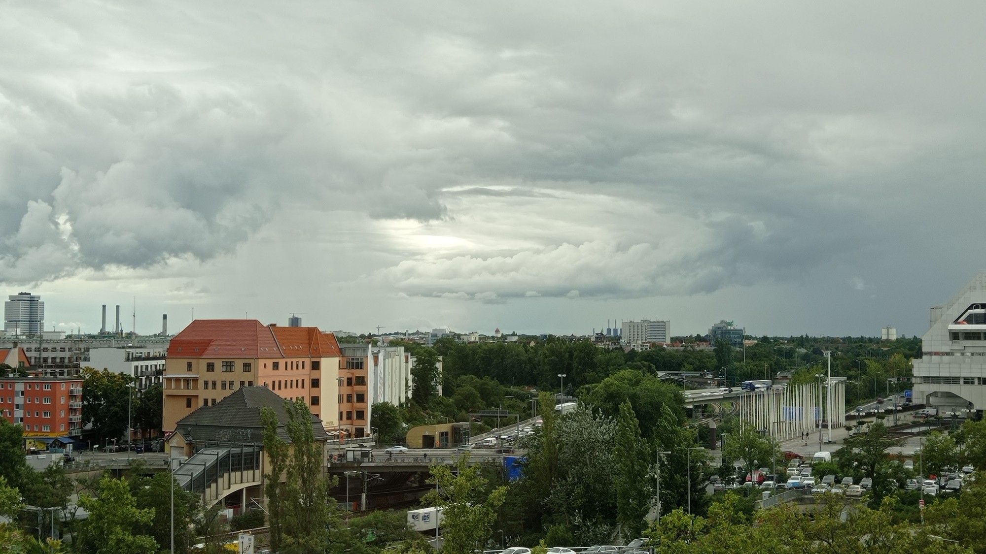 Die obere Hälfte zeigt eine apokalyptisch wirkende Wolkenstruktur in deren Zentrum ein heller, kreisförmig wirkender Kern ist. Die untere Hälfte zeigt einen kleinen Teil von Charlottenburg, grüne Bäume, verschiedene Gebäude. Ganz rechts vom Bild ist ein Teil des ICC zu sehen.