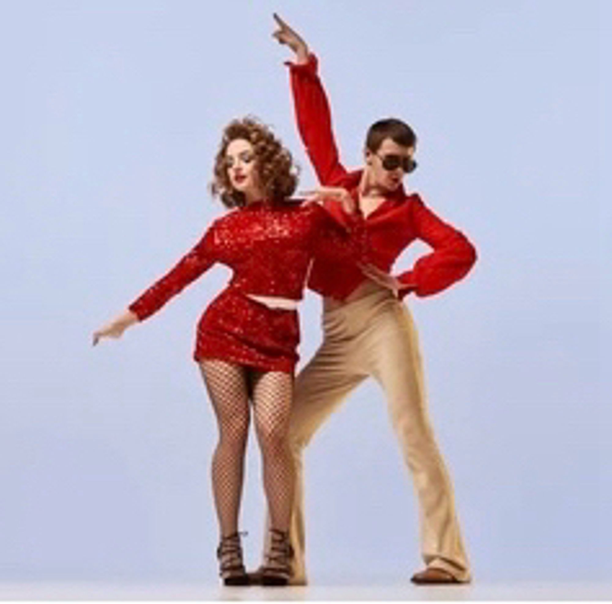 Two dancers in red. One is also wearing tan pants & sun glasses.