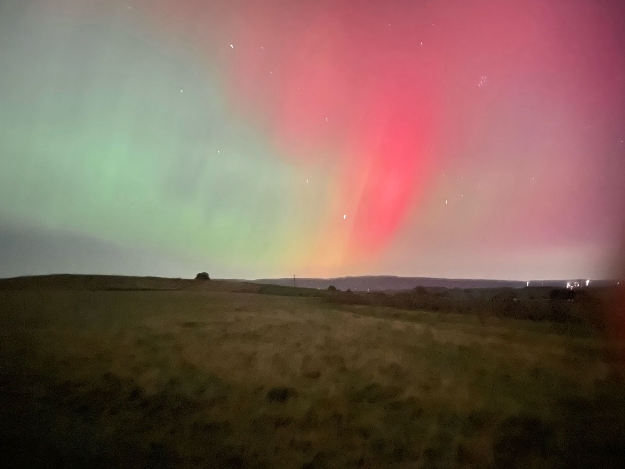 Vivid pink aurora in northern sky above moorland.