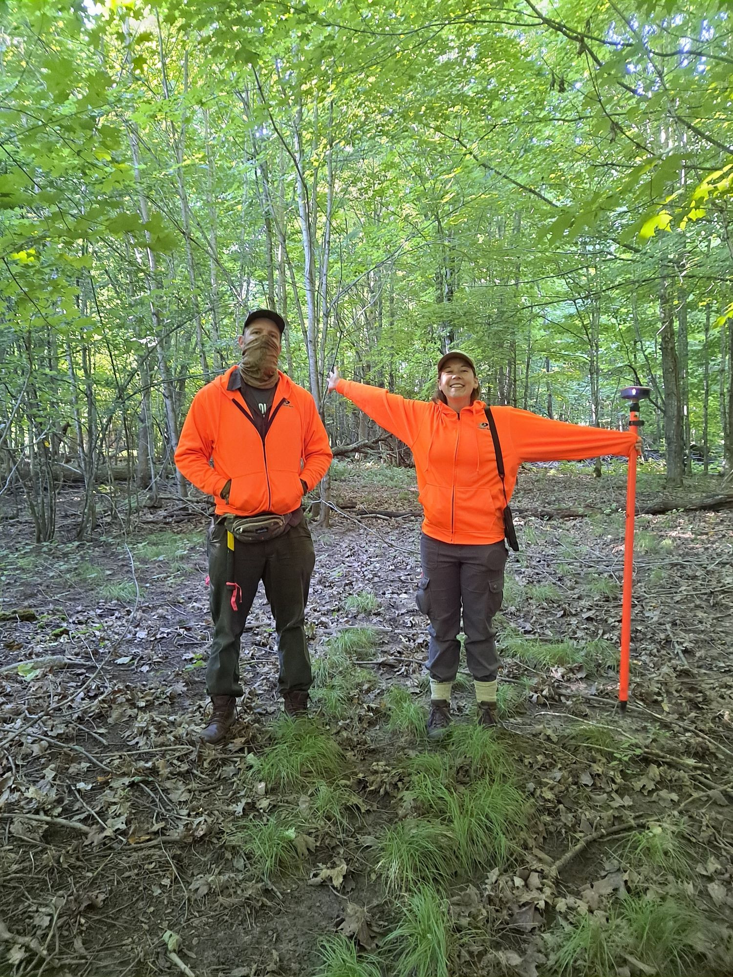 Two people in the forest, wearing orange sweaters.