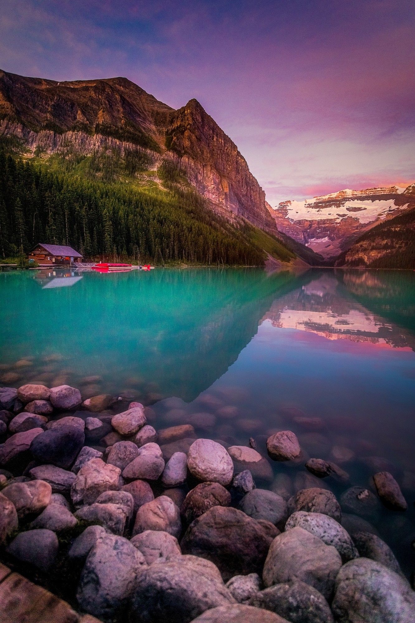 A cabin and canoes by a vibrantly colorful lake in Canada.