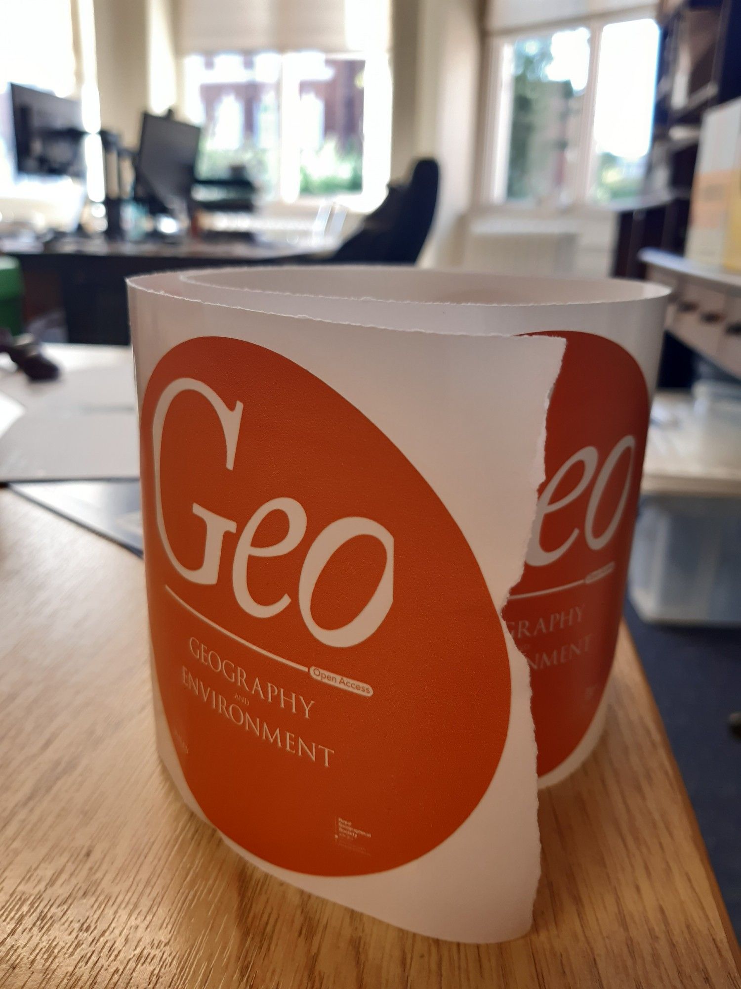 Photograph of a roll of round orange stickers with 'Geo: Geography and Environment' on them in white.