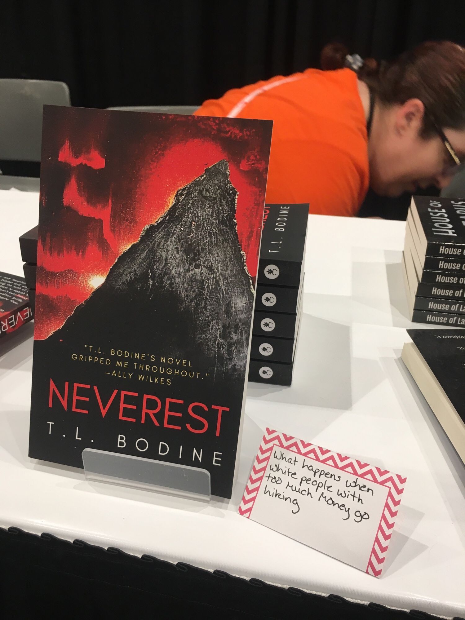 My book Neverest with a sign beside it reading “what happens when write people with too much money go hiking”