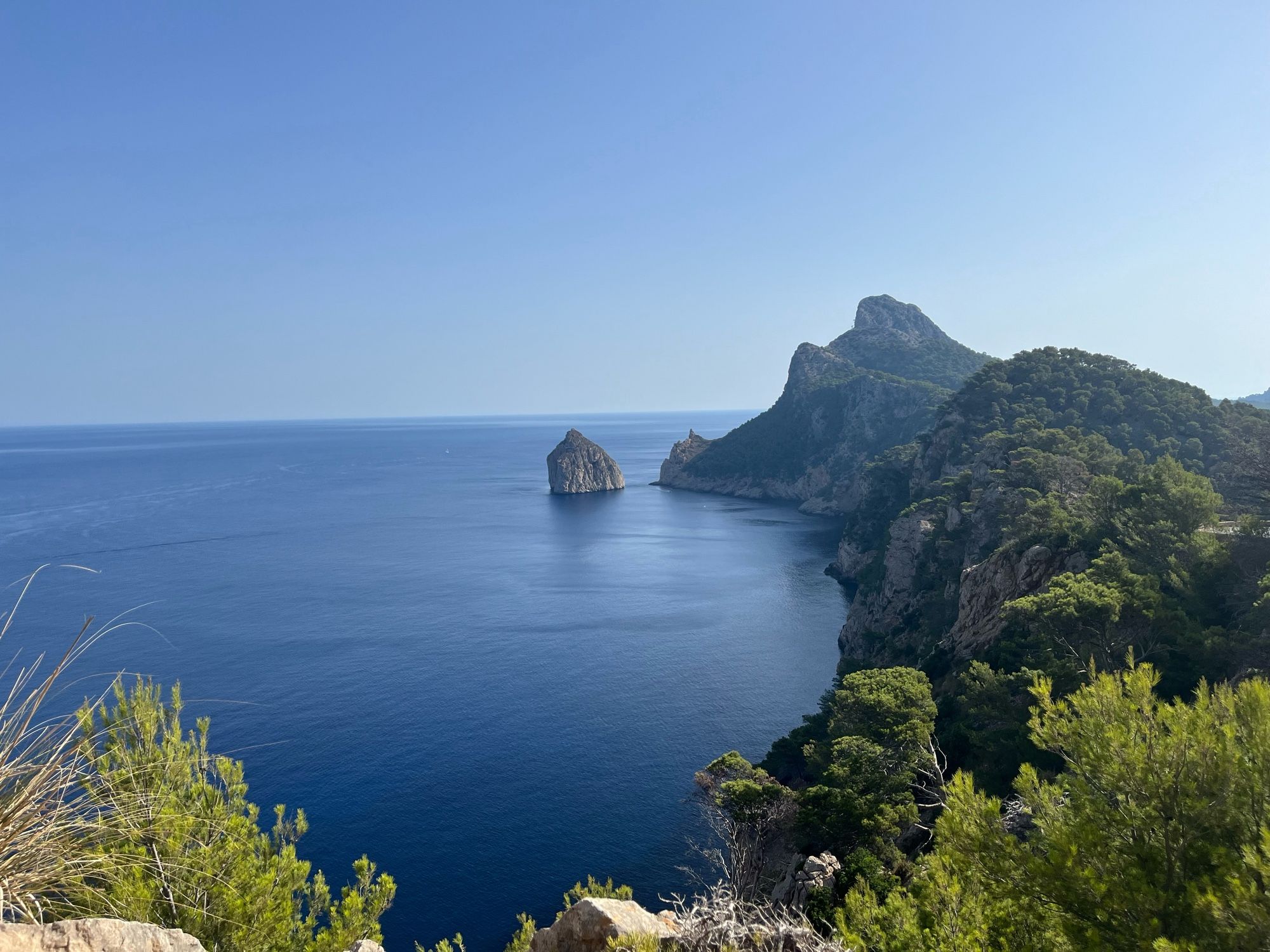 One of the spectacular views along the road out to the Formentor Lighthouse in Mallorca. The photo shows vegetation above dark sea and clear blue skies.