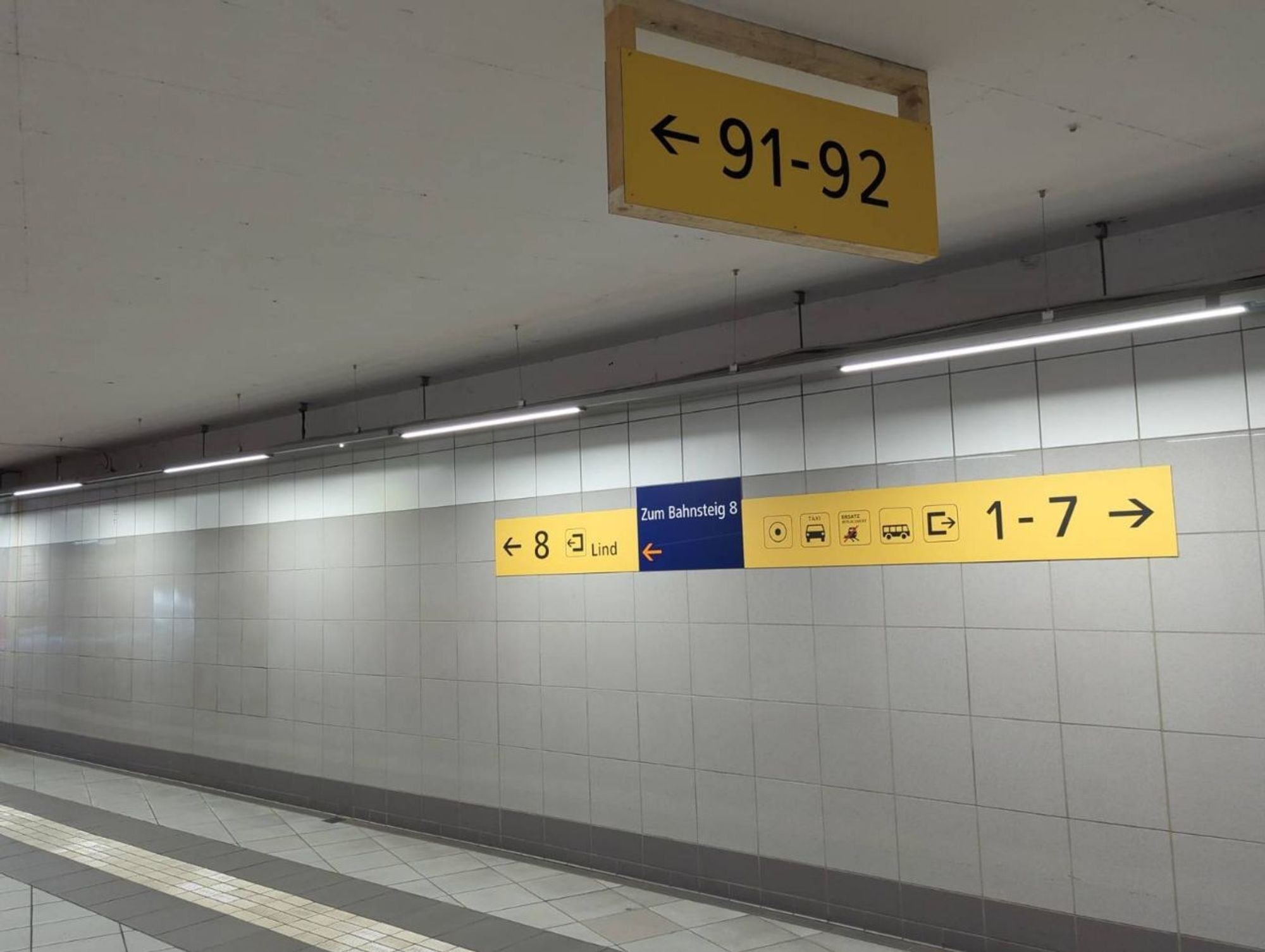 Ein kahler Gang mit Fliesenboden und -Wänden im Bahnhof Villach Hbf.

Ein blaues Schild führt zum Bahnsteig 8. Gelbe Baustellenbeschilderung ebenfalls zum Bahnsteig 8, Ausgang Lind, sowie zu den Bahnsteigen 1 bis 7 und zum Bahnhofvorplatz.